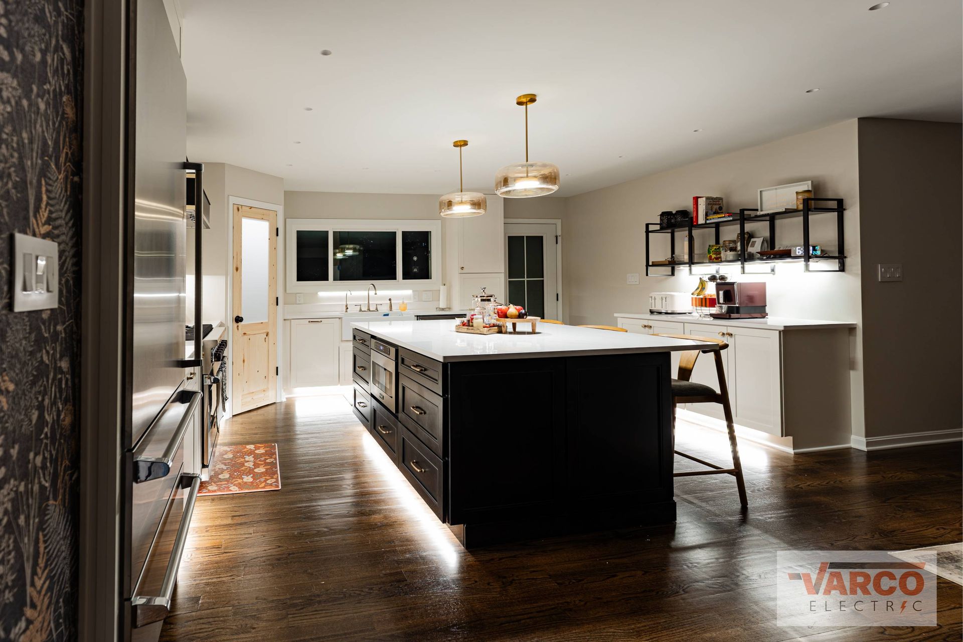 Modern kitchen with dark island, pendant lights, stainless appliances, and under-cabinet lighting.