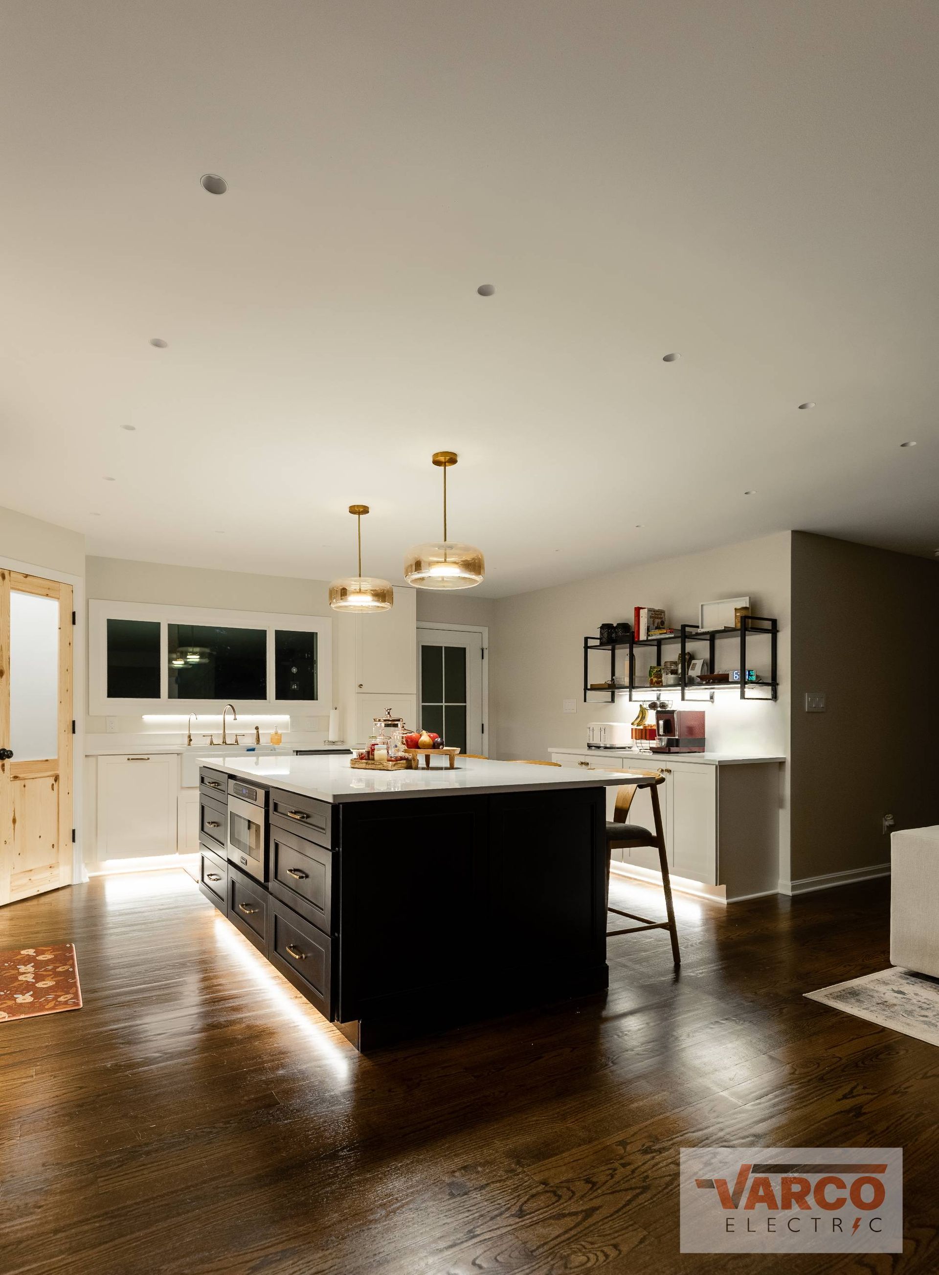Kitchen with dark wood island, white countertops, and wood floors. Gold pendant lights hang above.