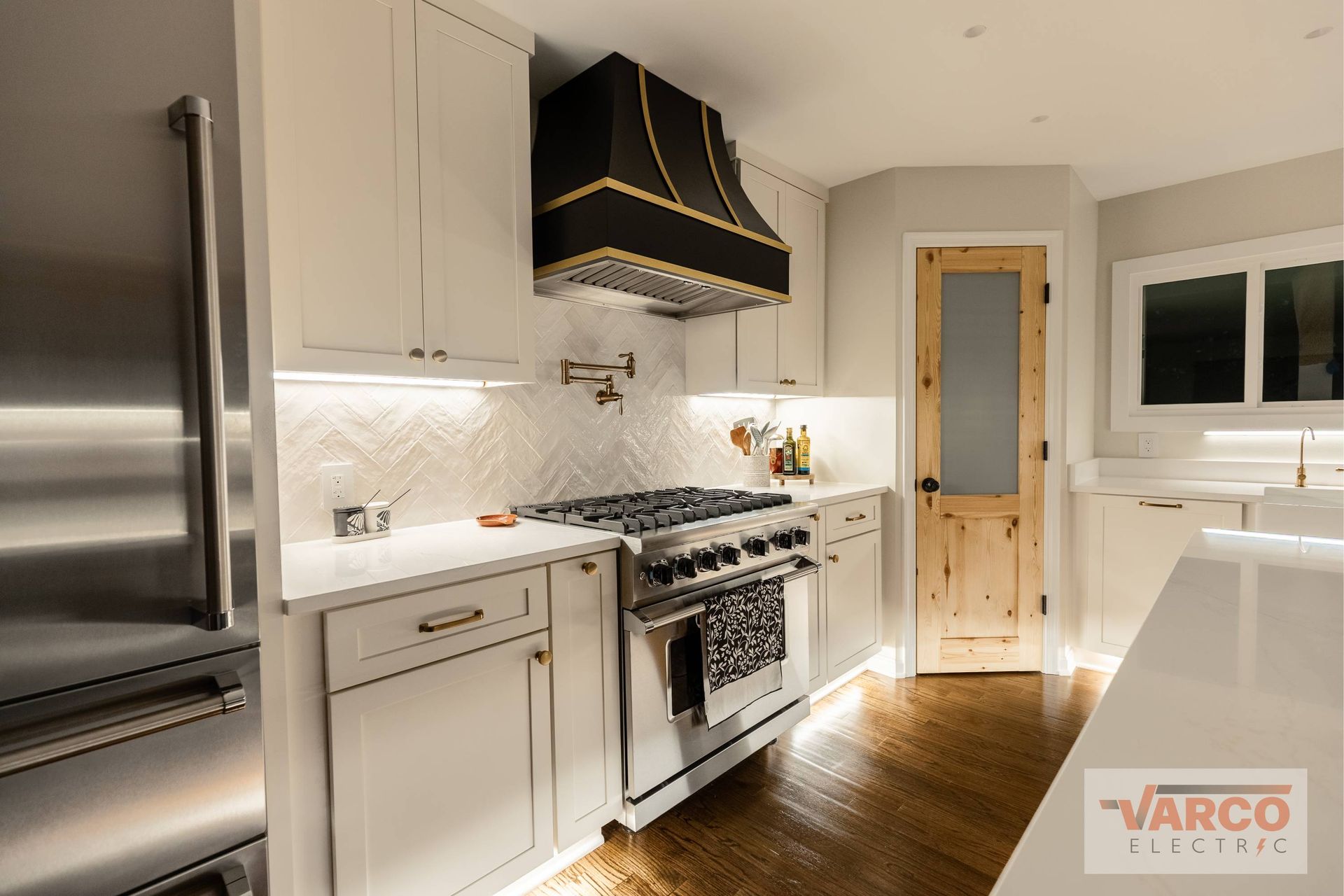 Modern kitchen with white cabinets, stainless steel appliances, black range hood, and wood door.