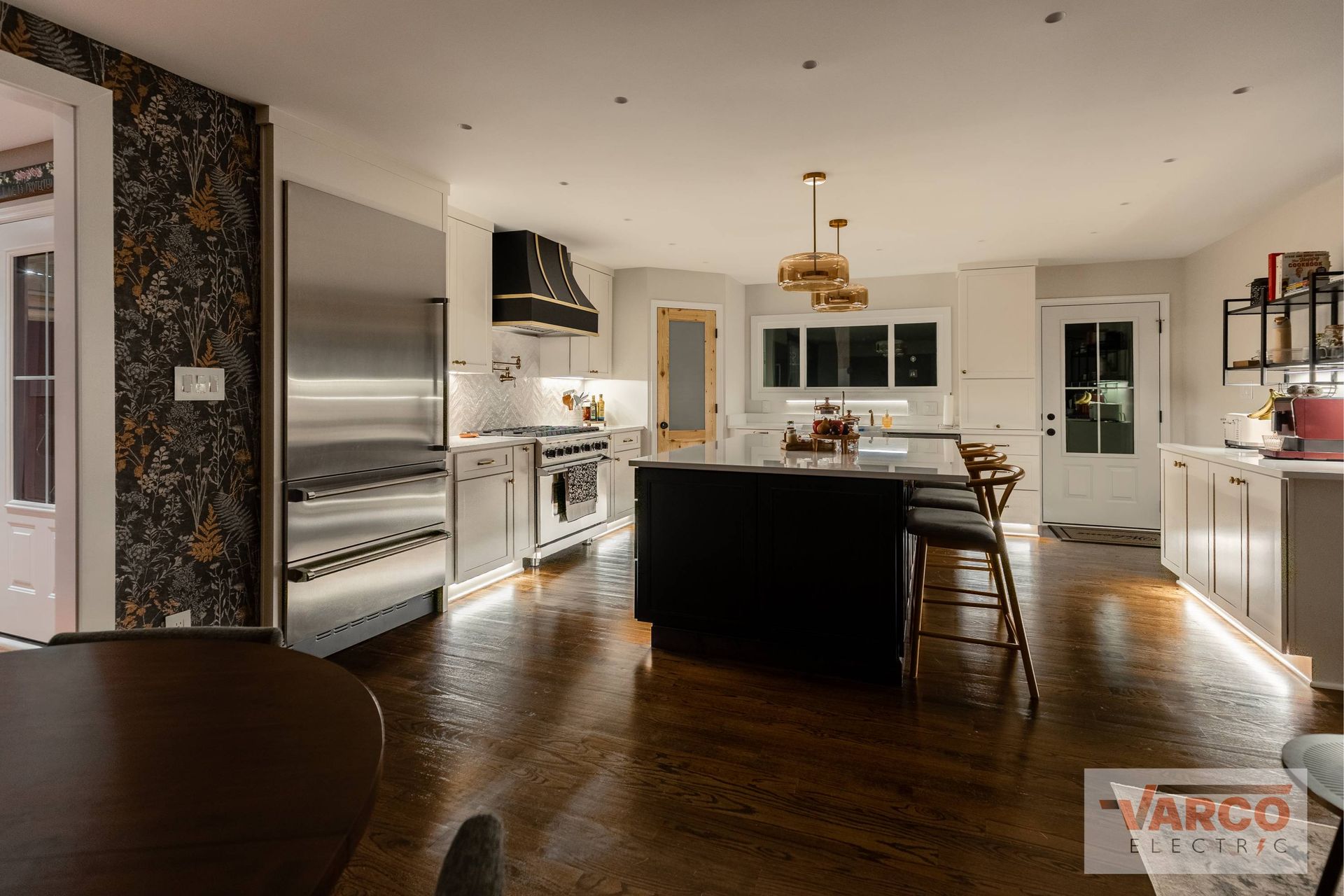 Well-lit modern kitchen with stainless steel appliances, dark island, and wooden floors.