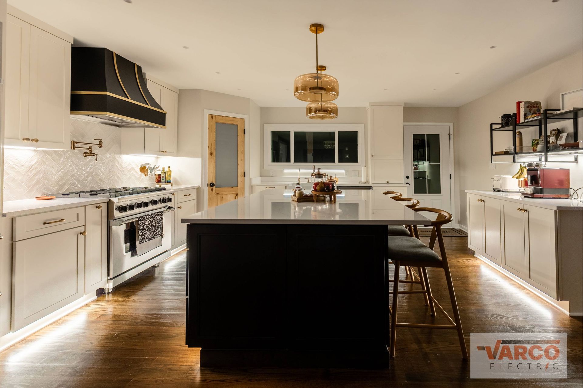 Modern kitchen with island, black accents, white cabinets, and wooden floors.