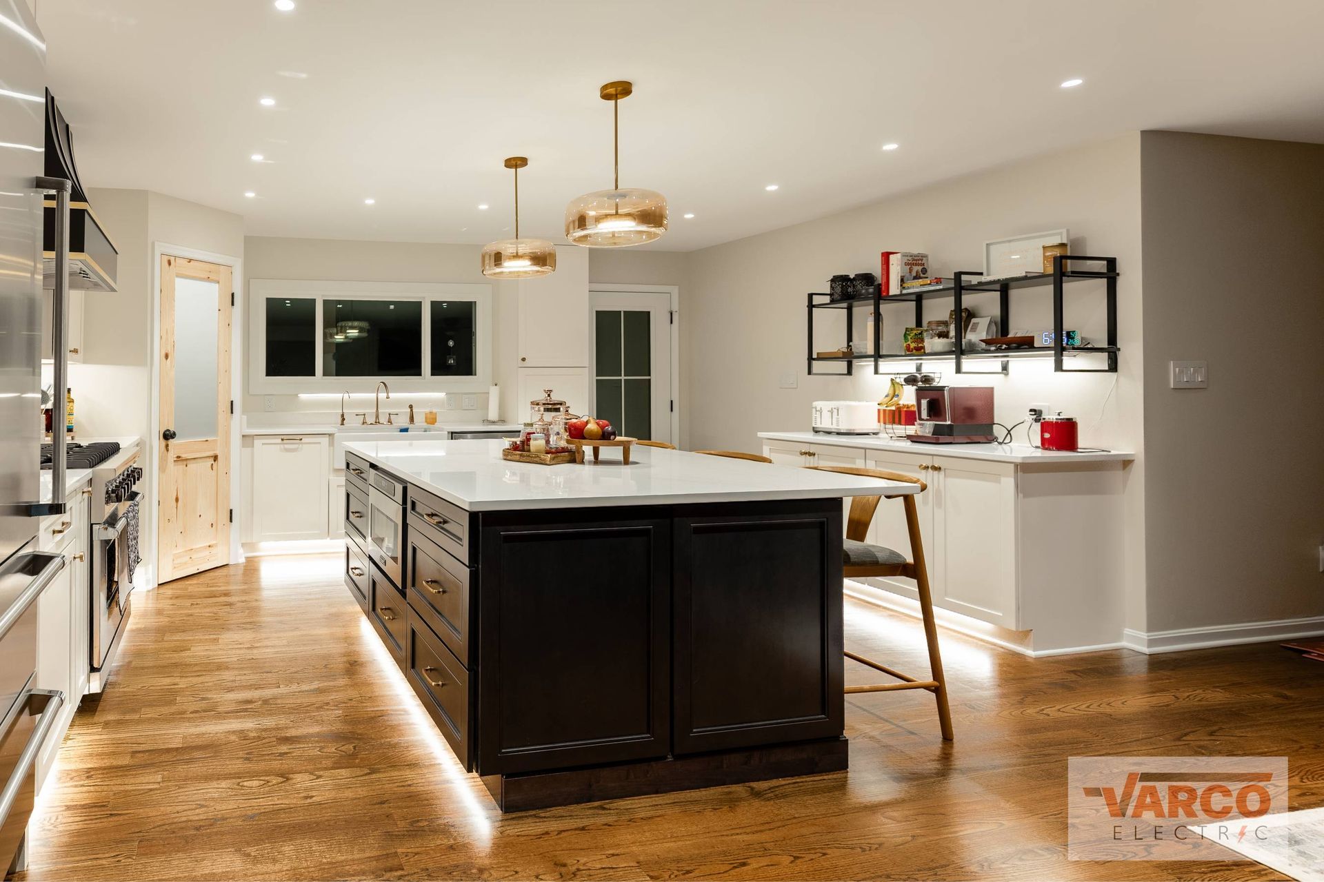 Modern kitchen with a black island, white countertops, and wooden floors.
