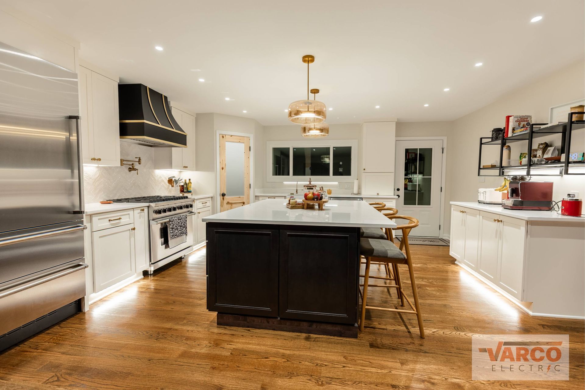 Modern kitchen with white cabinets, black island, stainless steel appliances, and gold accents.