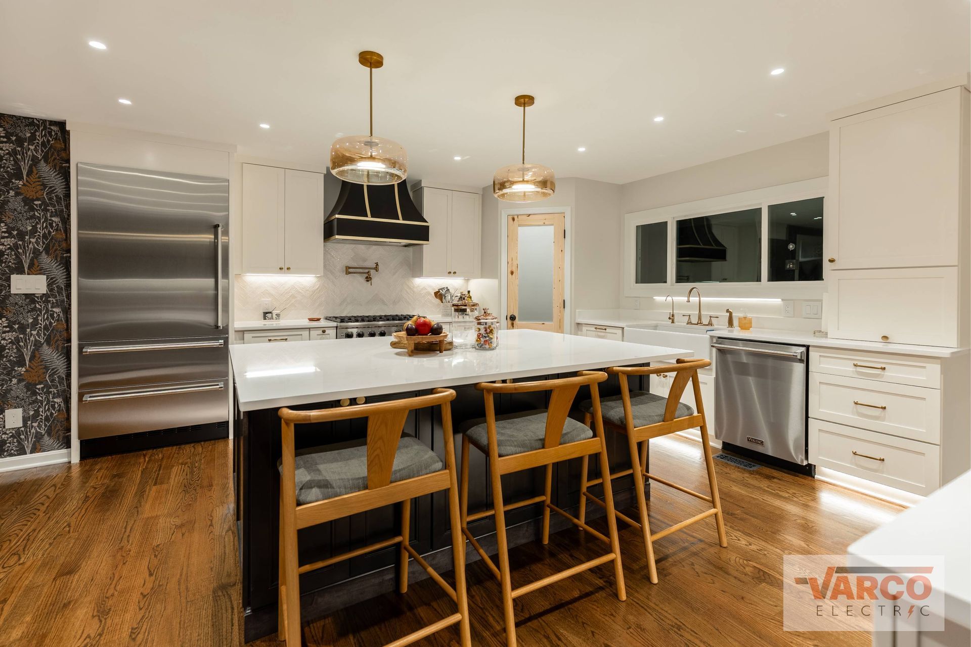 Modern kitchen with island, stools, stainless steel appliances, and white cabinets.