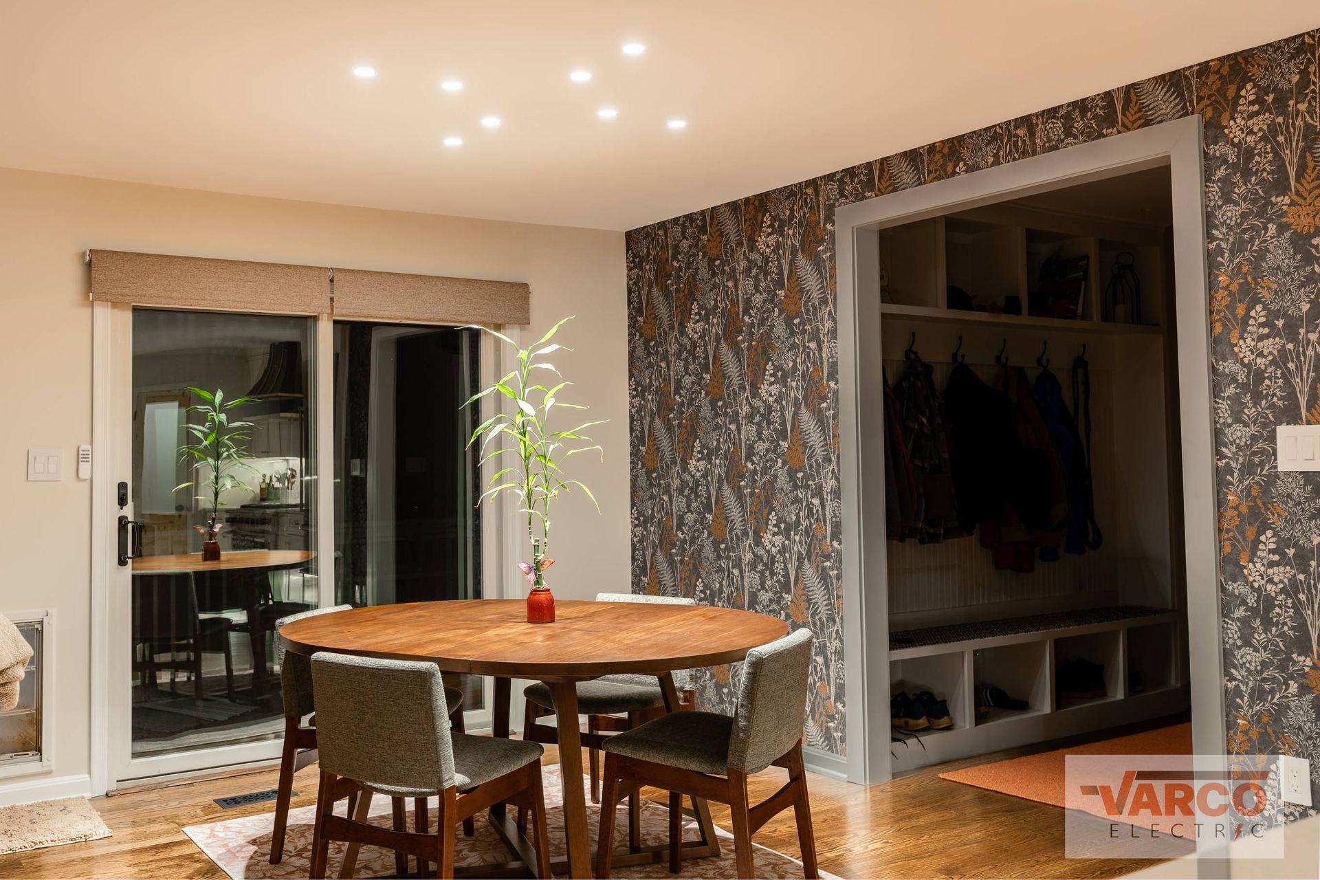 Dining room with round table, chairs, and coat closet with patterned wallpaper.