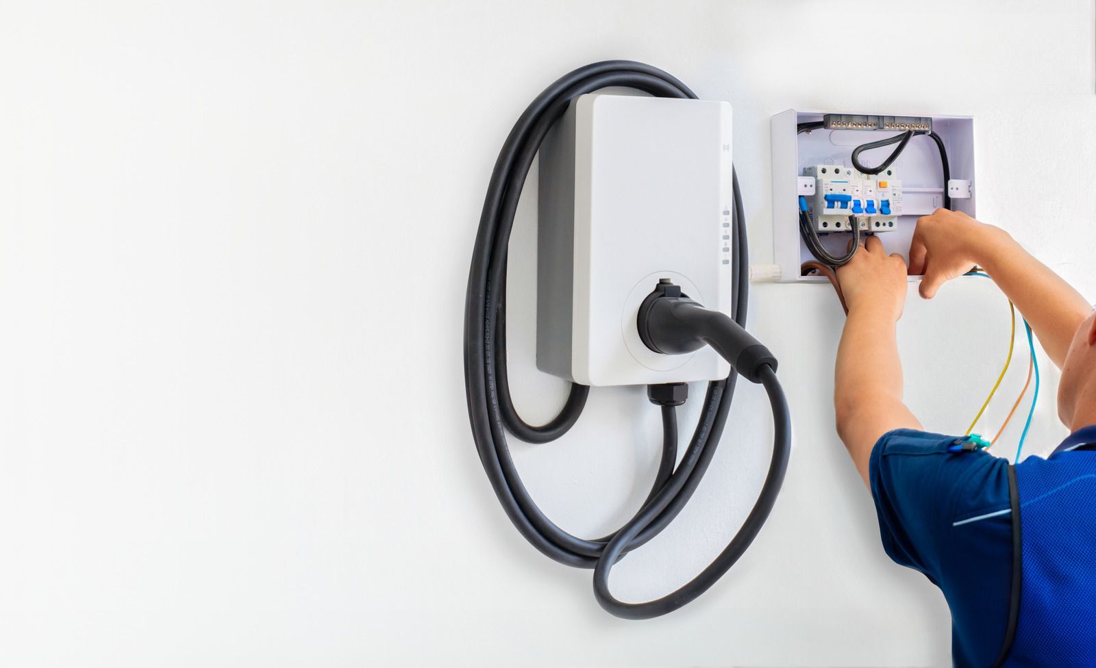 Person working on an electric vehicle charger's electrical box, mounted on a white wall.