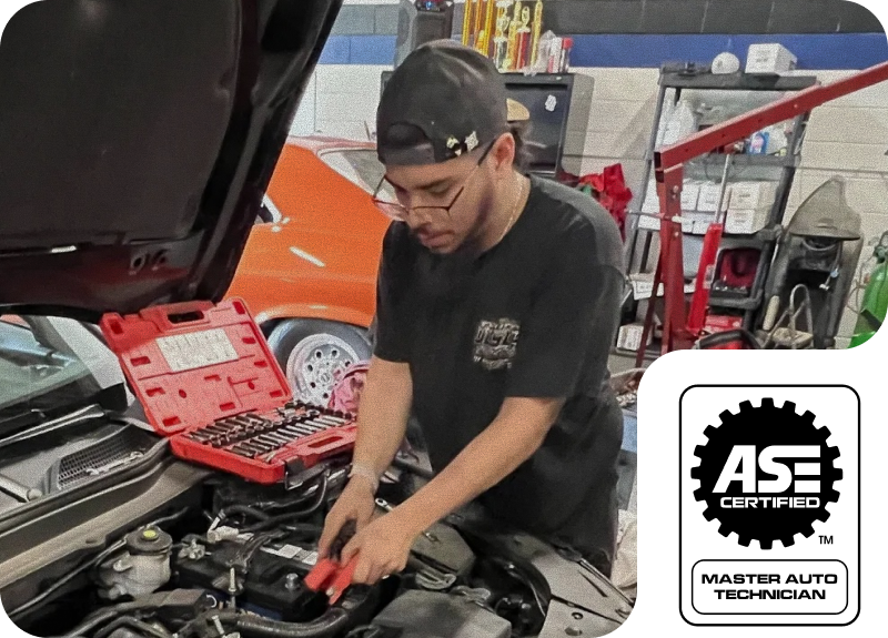 Mechanic working on a car engine in a garage; red toolbox open. ASE Certified logo. | Ashten's Total Auto Care