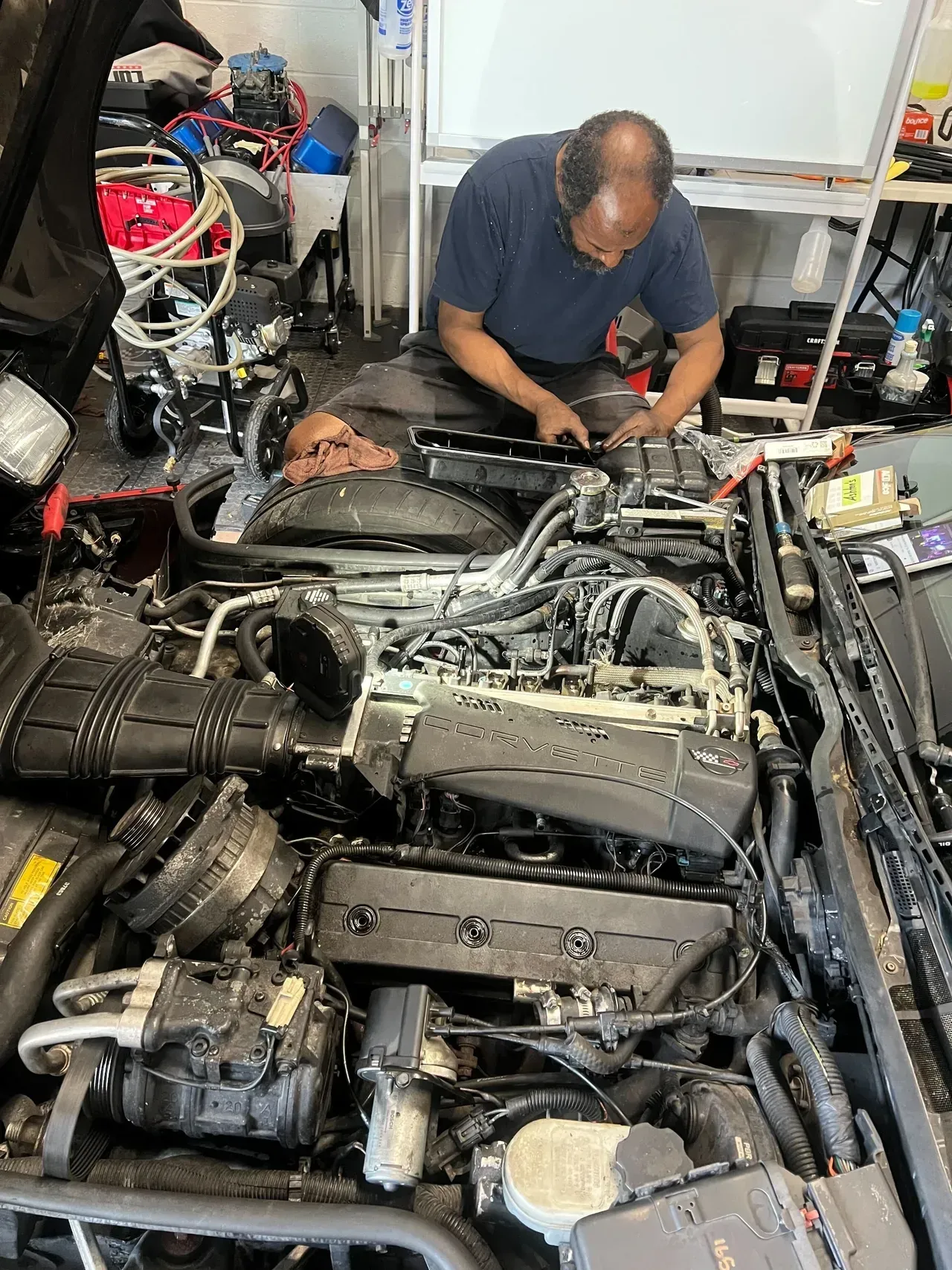 Man working on car engine, leaning in with tools. Engine is black, in a garage. | Ashten's Total Auto Care