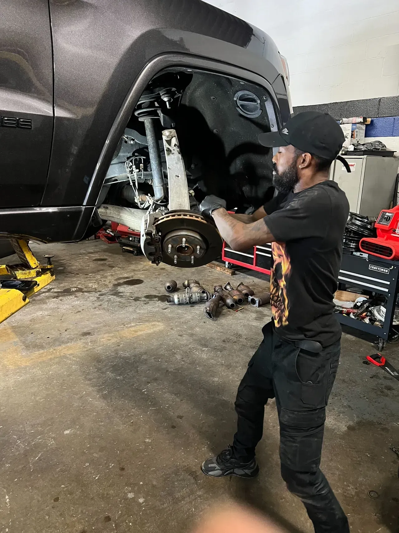 Mechanic working on a car in a garage, removing a wheel. | Ashten's Total Auto Care