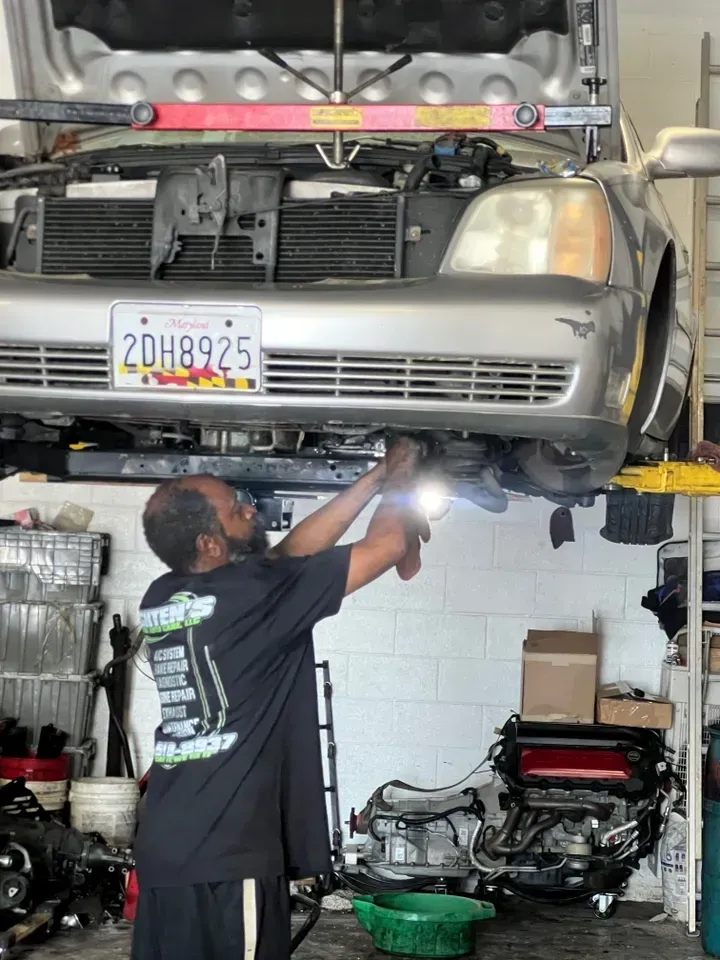 Mechanic working on a car in a shop, holding a light. The car is elevated. | Ashten's Total Auto Care