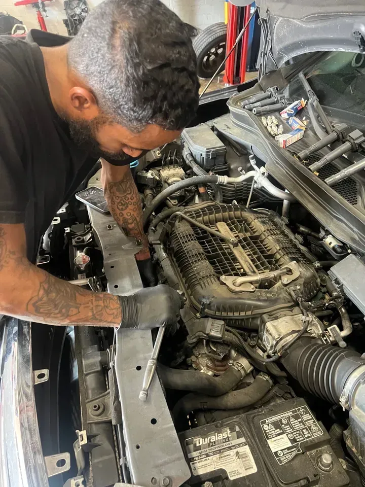 Mechanic working on a car engine; uses tools. Black gloves and tattoos are visible. | Ashten's Total Auto Care