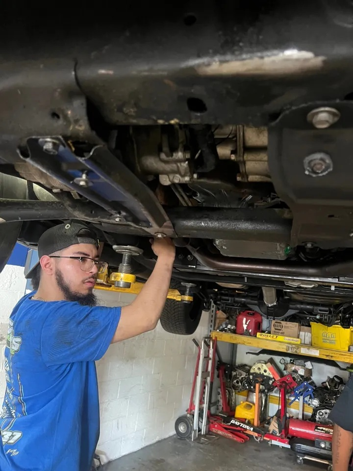 Mechanic working under a car, reaching up to work on the undercarriage in a garage with tools and equipment. | Ashten's Total Auto Care
