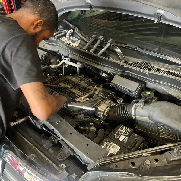 Mechanic working on a car engine with the hood open. | Ashten's Total Auto Care