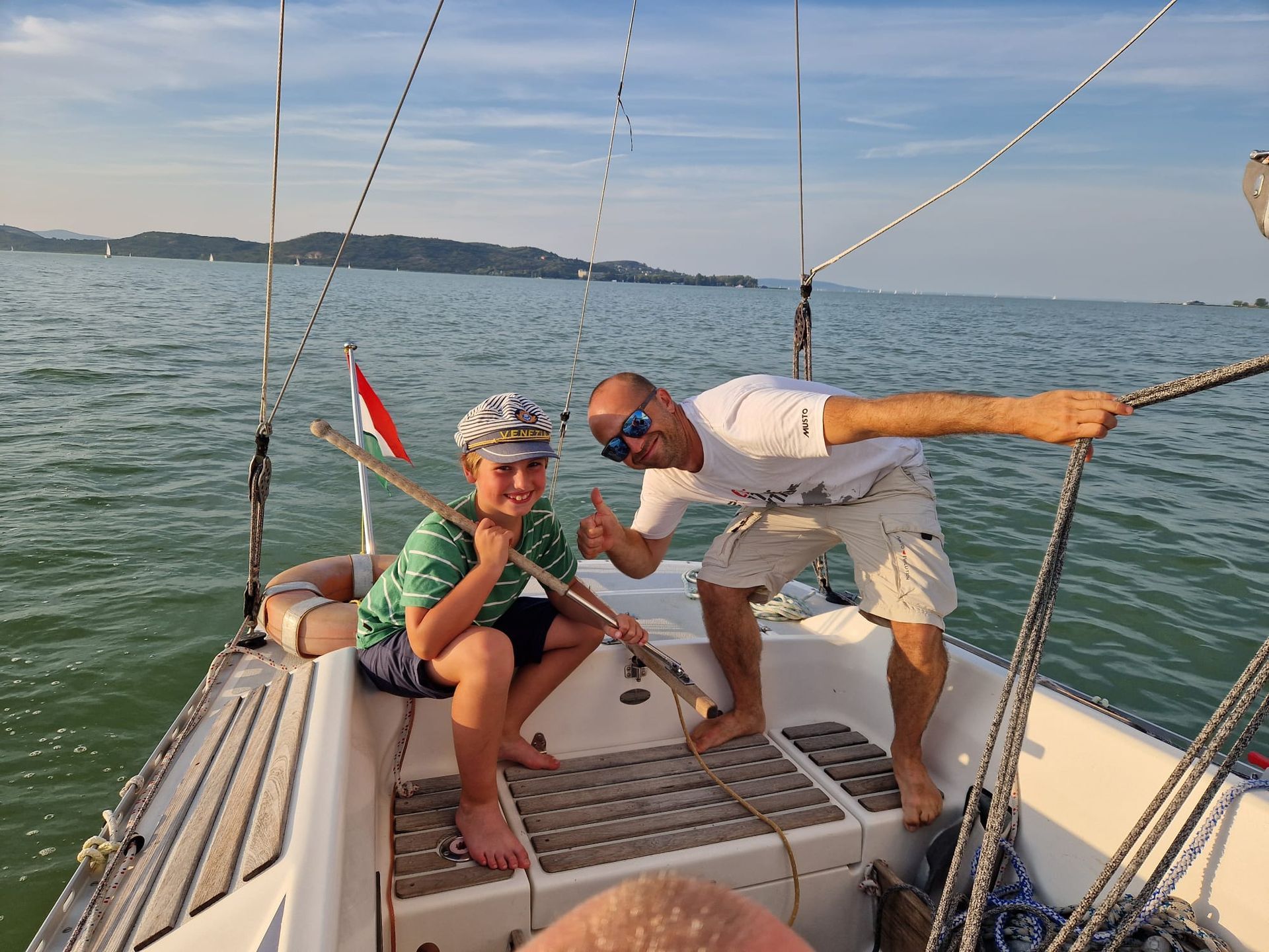 Man and boy on sailboat, smiling, giving thumbs up. Ocean backdrop.