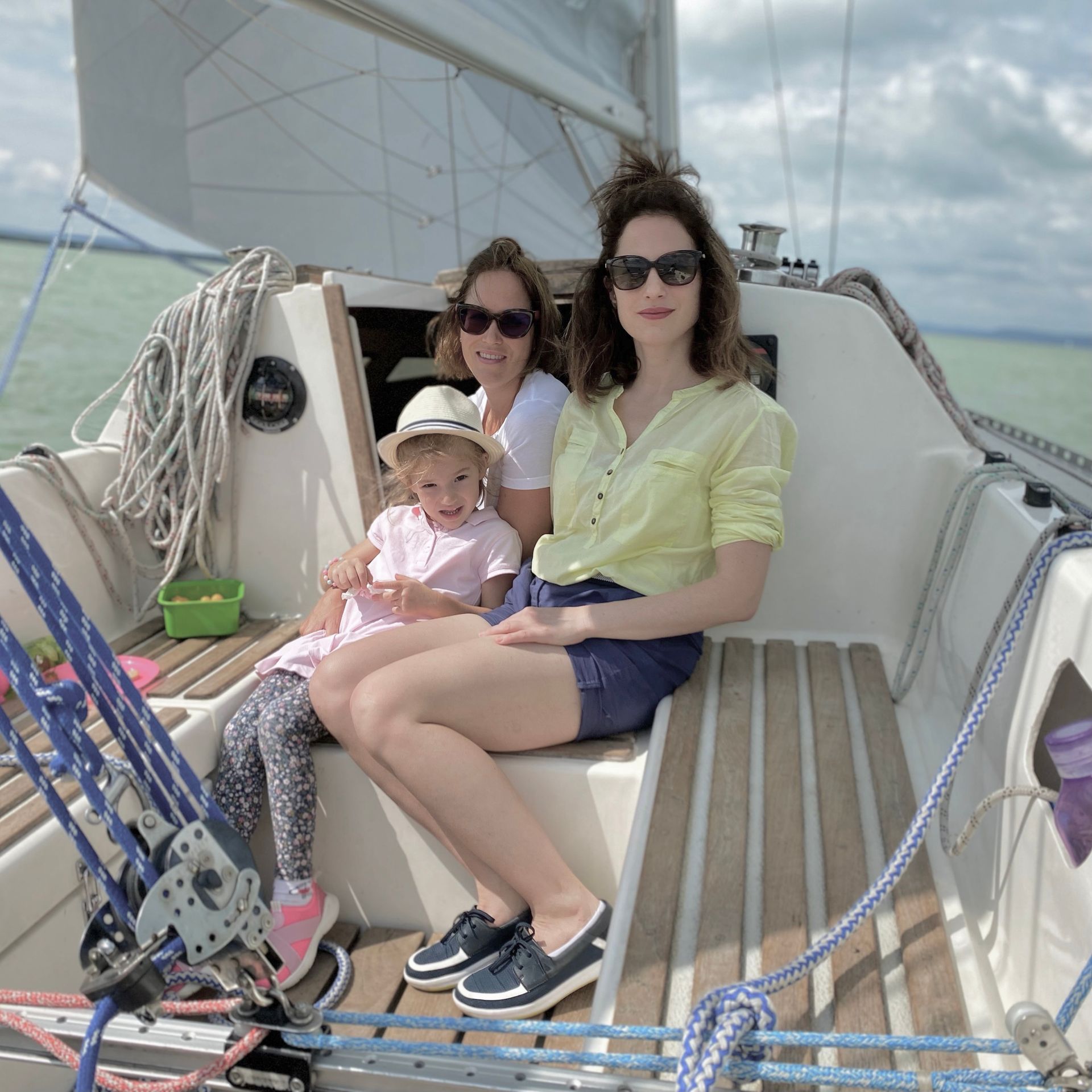Three people, including a child, on a sailboat, smiling.