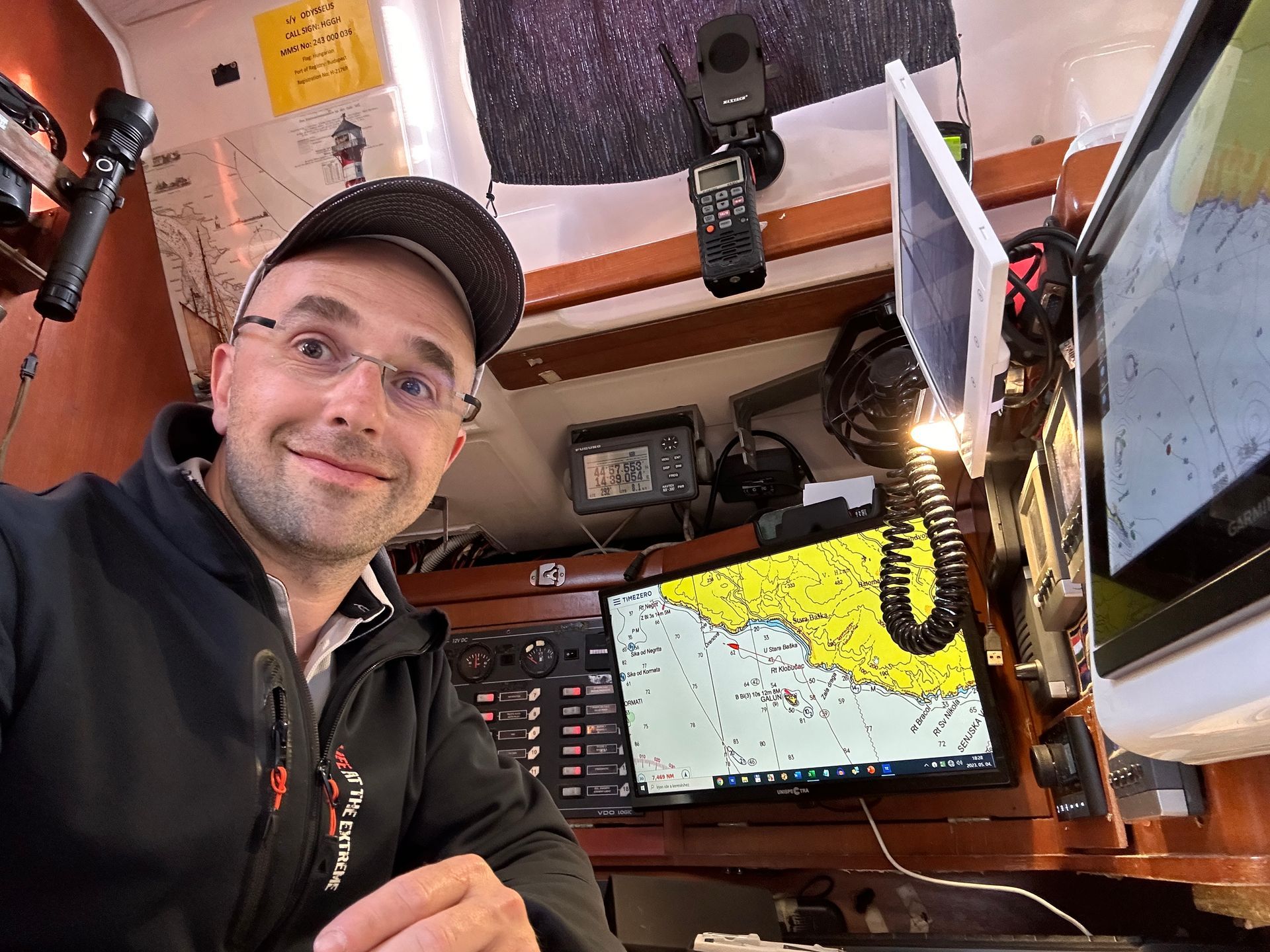 Man in a boat's cockpit, smiling, wearing a cap, surrounded by navigation screens and equipment.