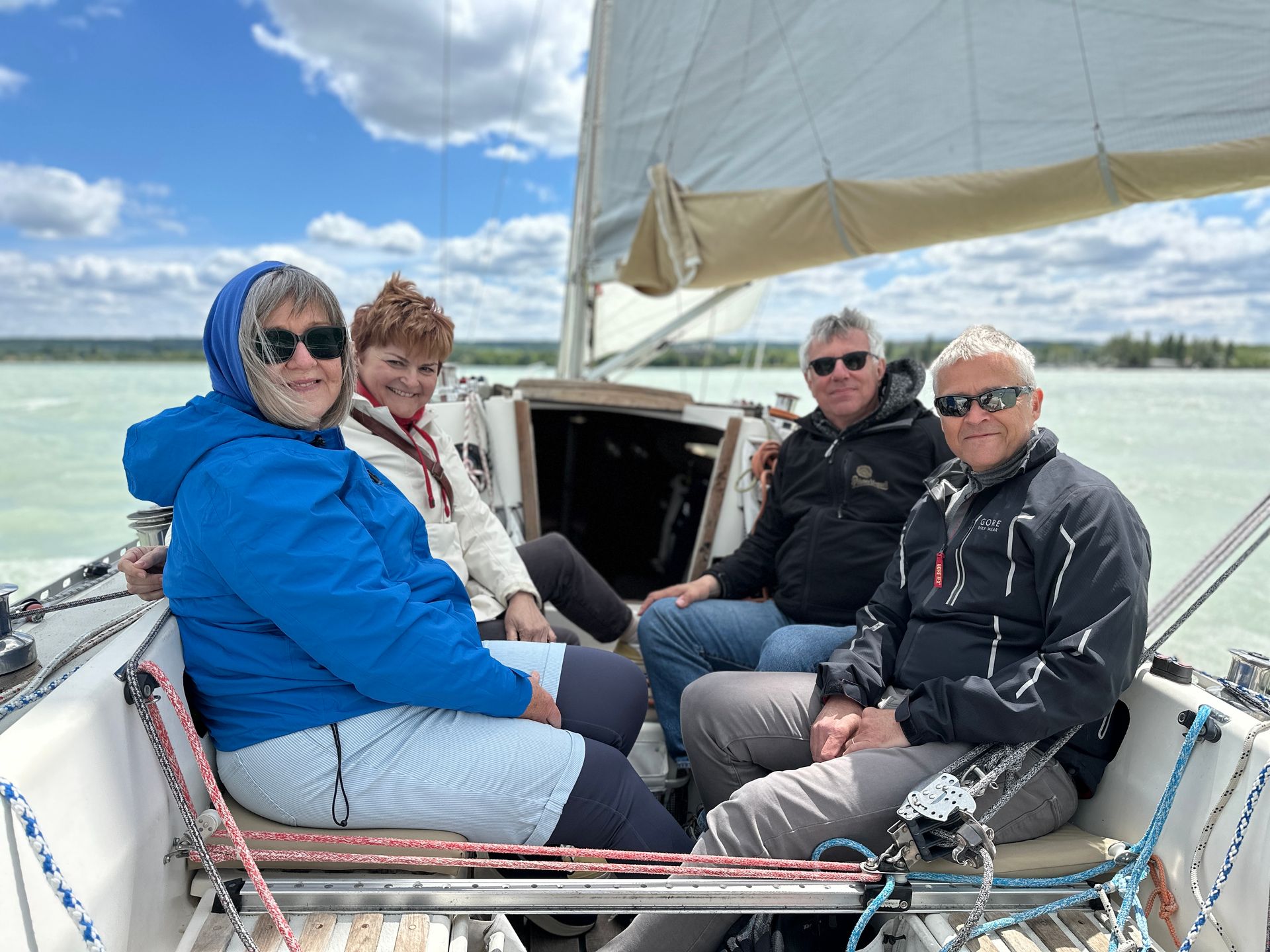 Four people sailing on a boat; sunny day with blue sky and light green water.