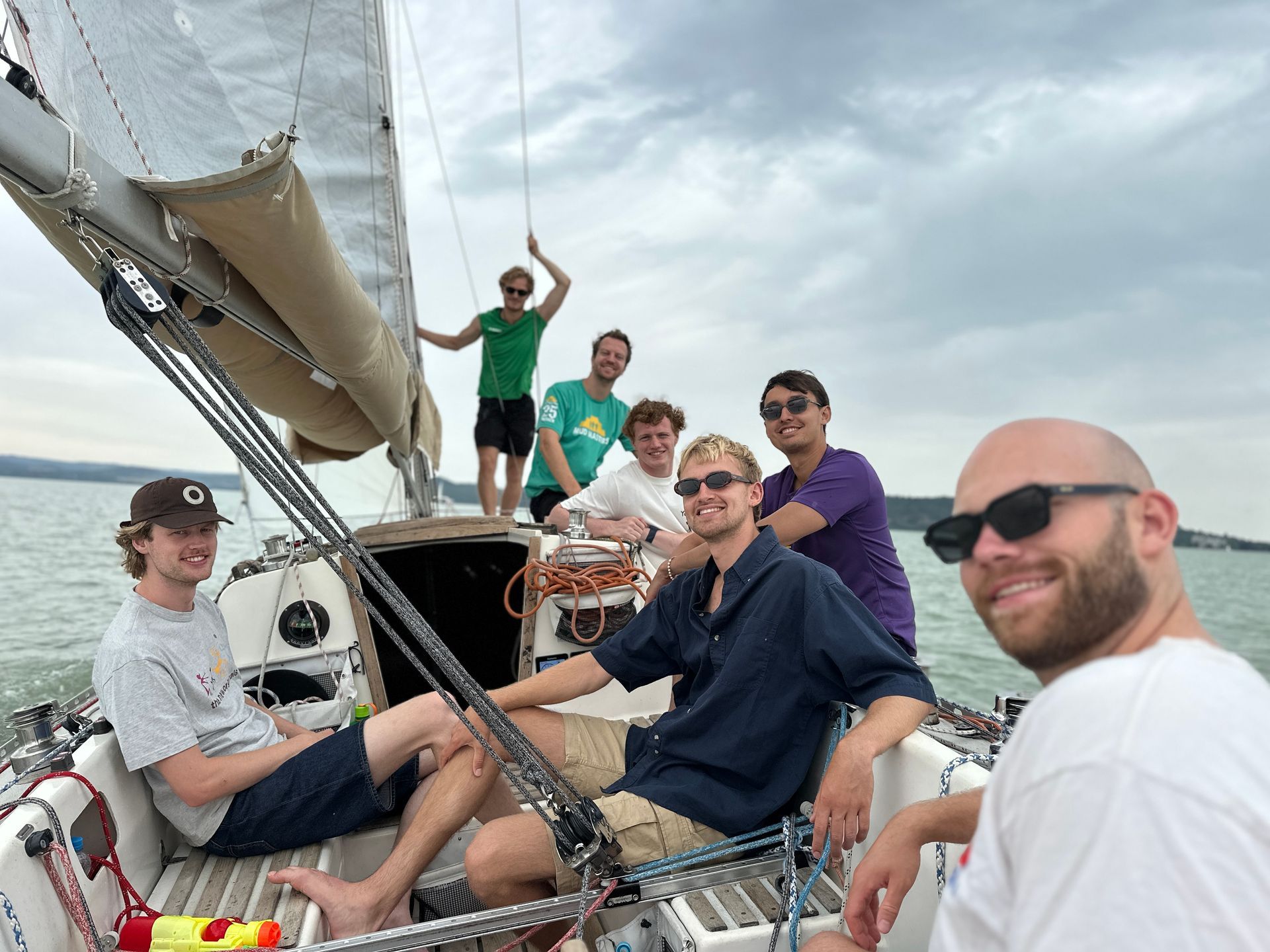 Group of friends smiling on a sailboat under a cloudy sky.
