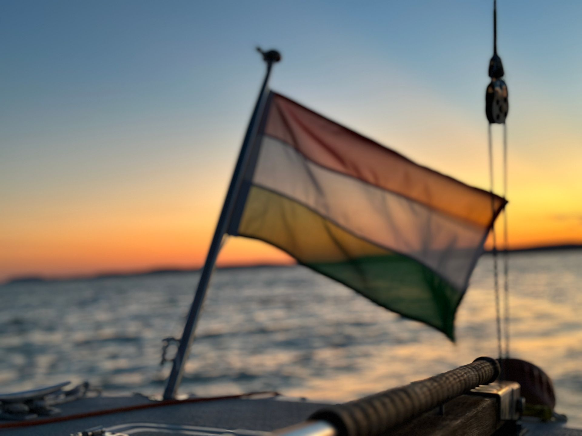 Hungarian flag waving on a boat at sunset over the water; orange, white, and green.