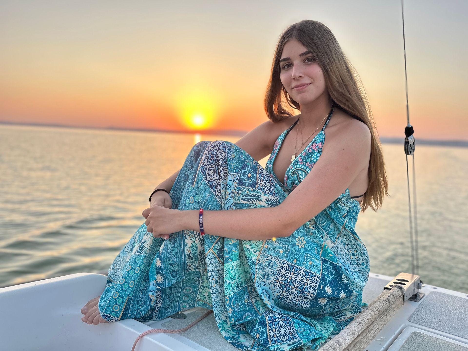 Woman in blue dress on boat at sunset, arms crossed, smiling.