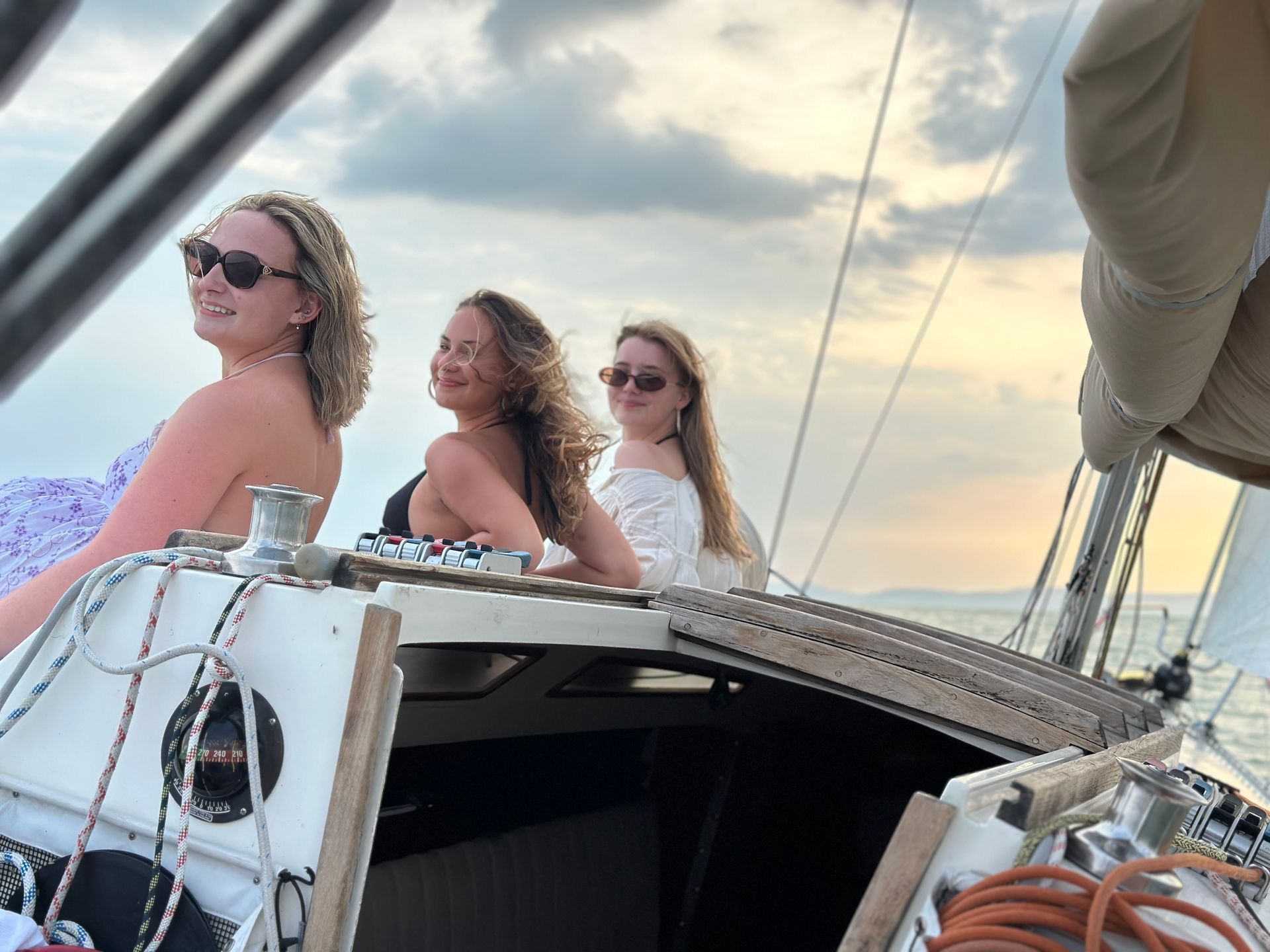 Three women on a sailboat, smiling, at sunset.