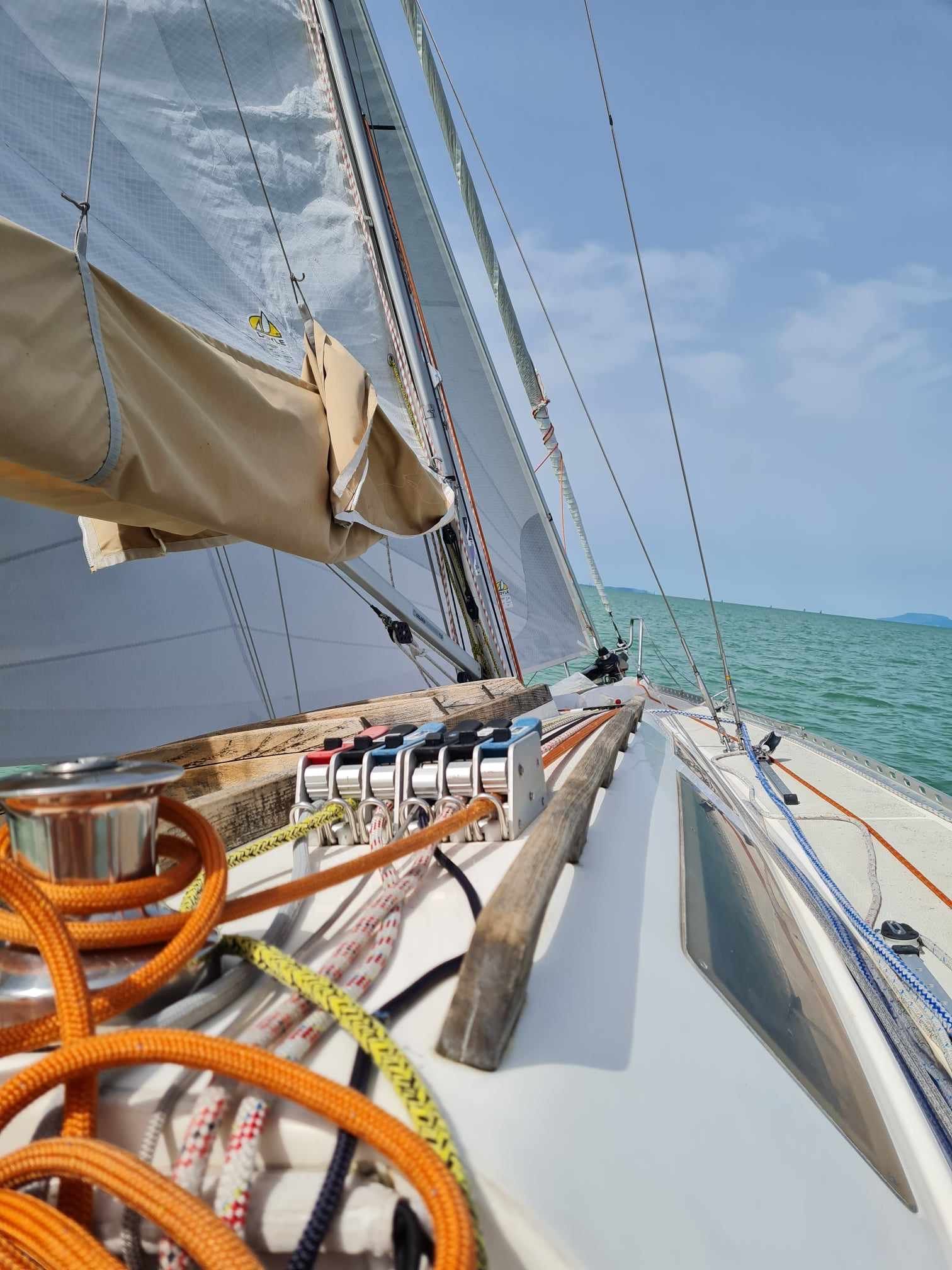Sailboat sailing on a bright day, view from deck with ropes, sails, and turquoise water.
