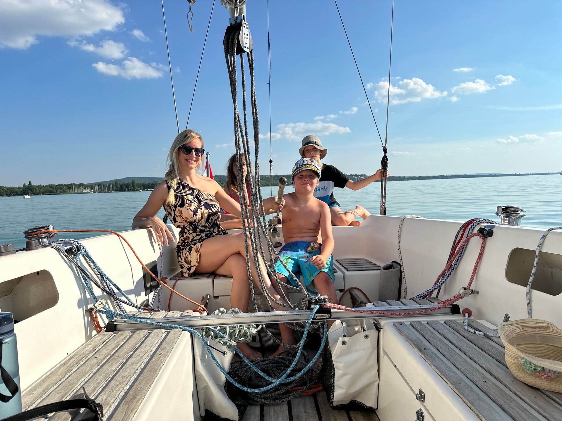 Family sailing on a sunny day: woman, child, and others on a boat with clear skies and water.