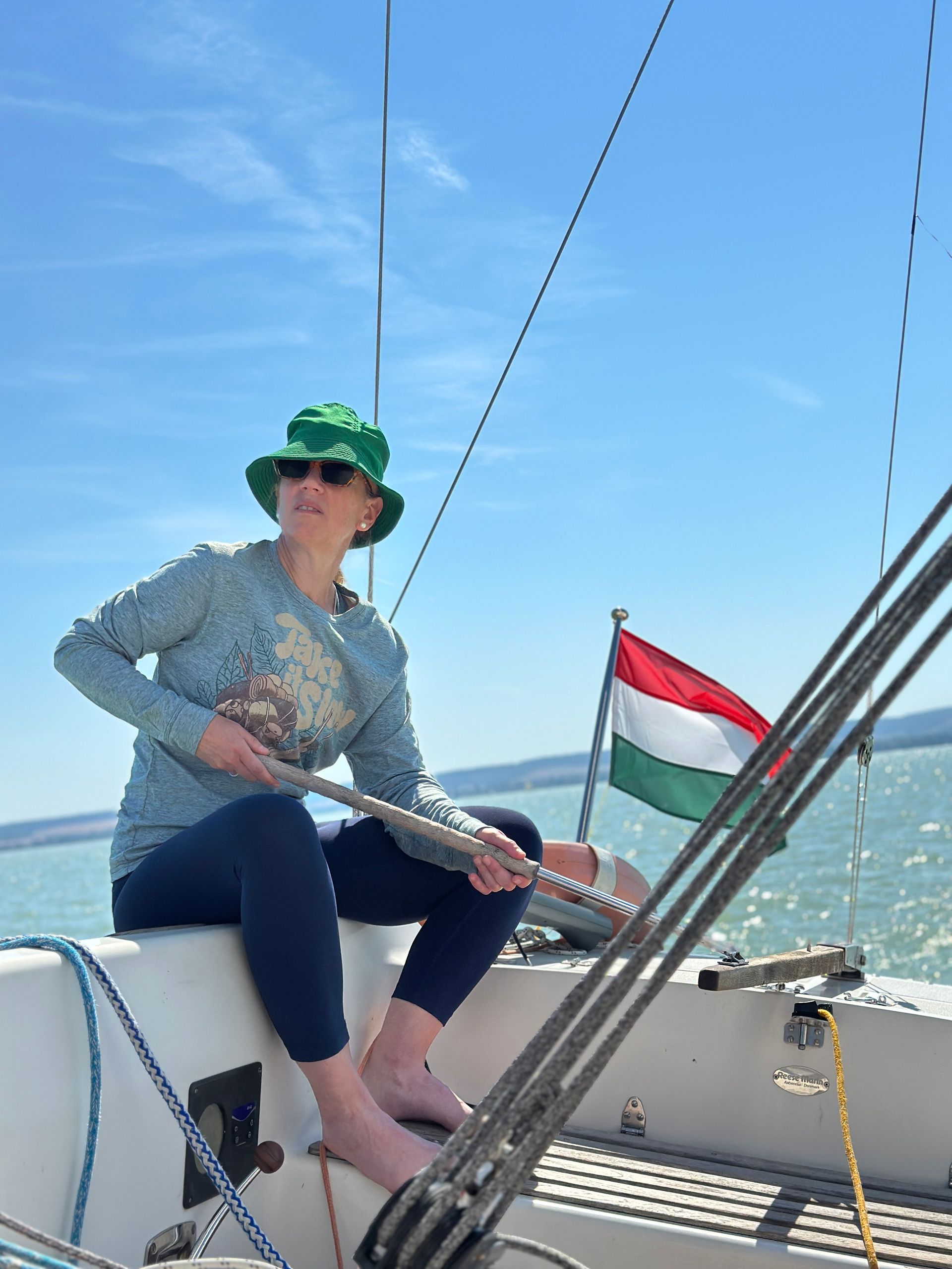 Person wearing green hat sailing on a boat, Hungary flag in the background.