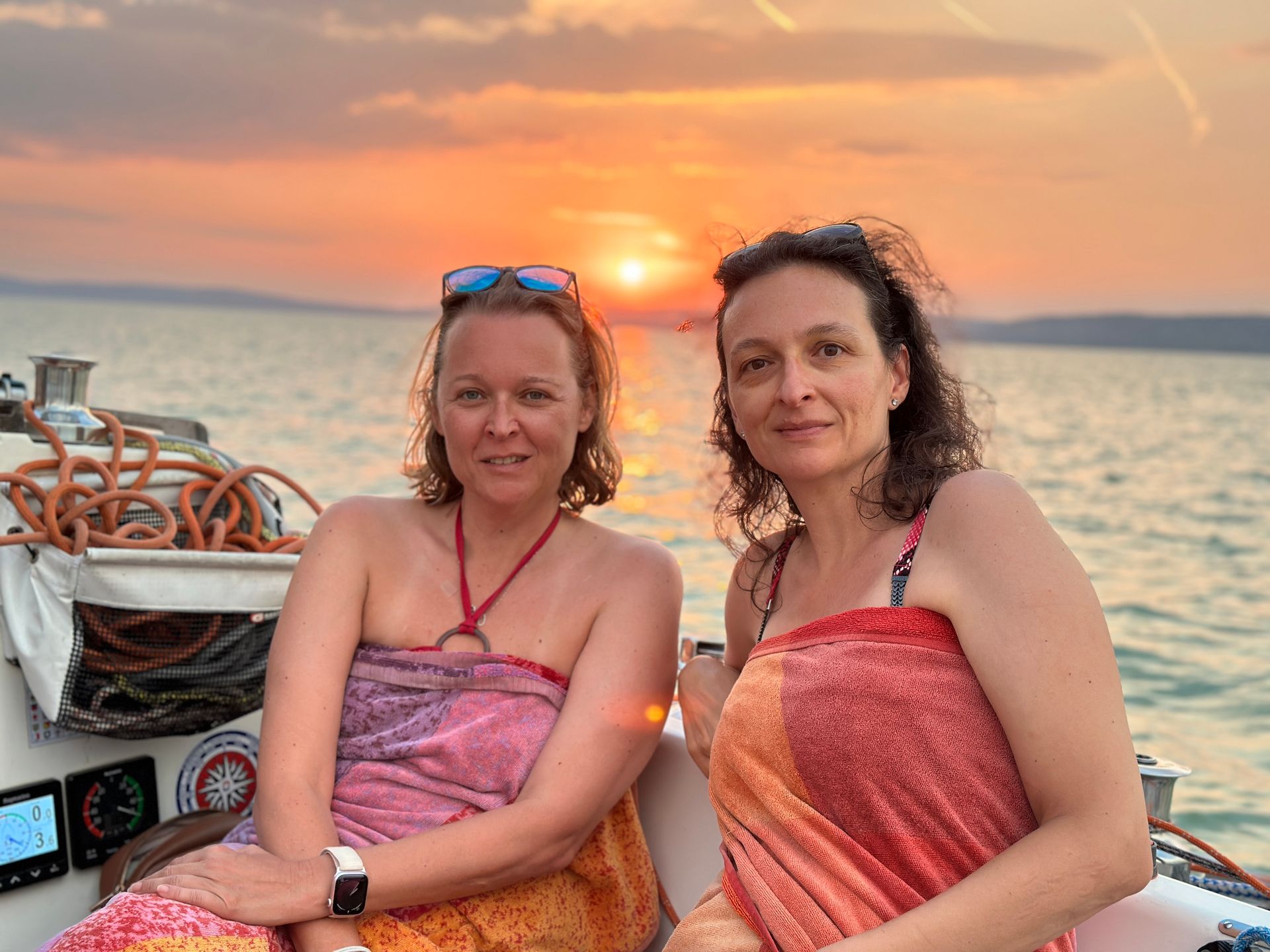 Two women on a boat at sunset, wrapped in colorful fabrics.