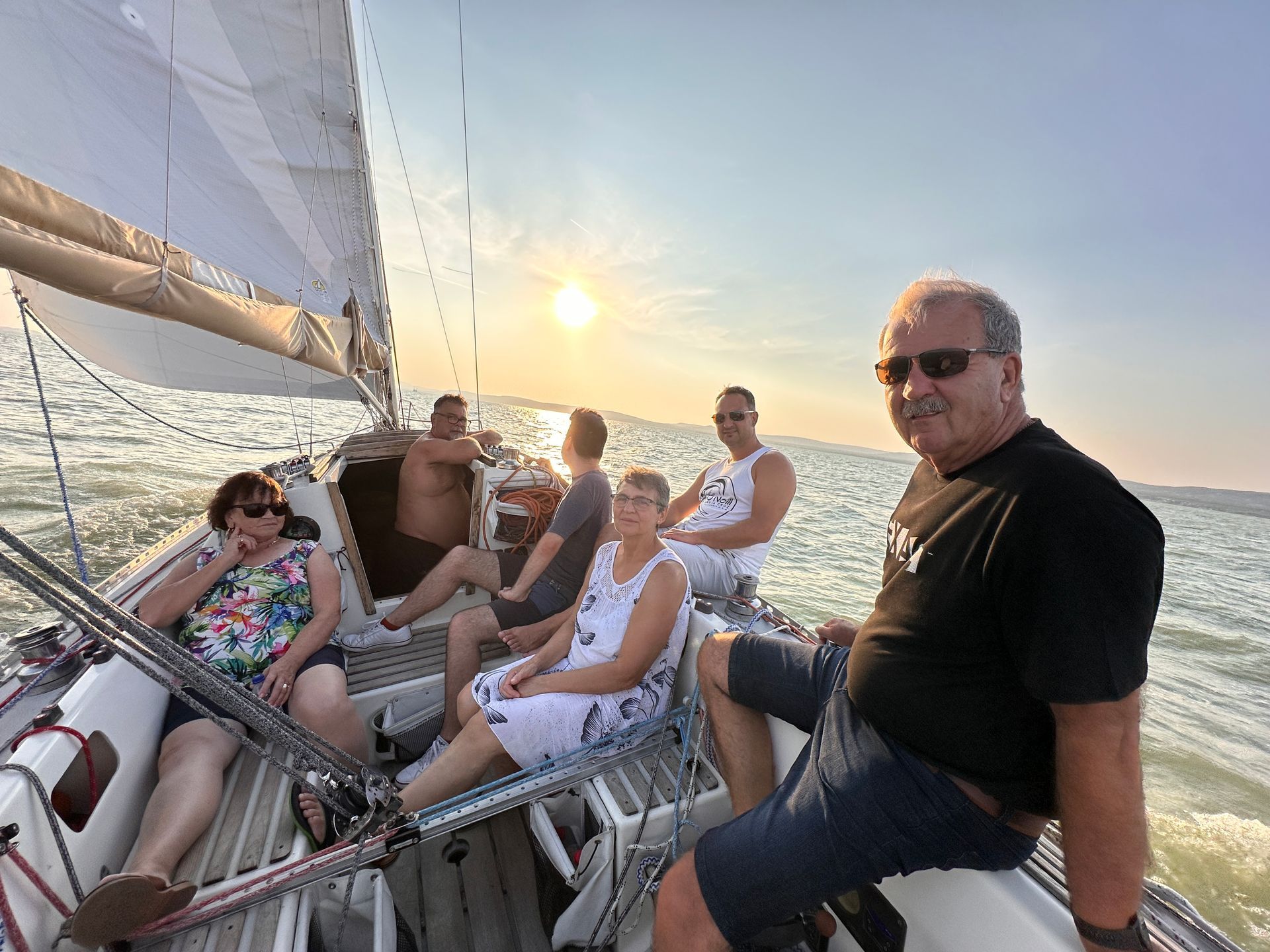 People sailing on a boat, with the sun setting in the background.