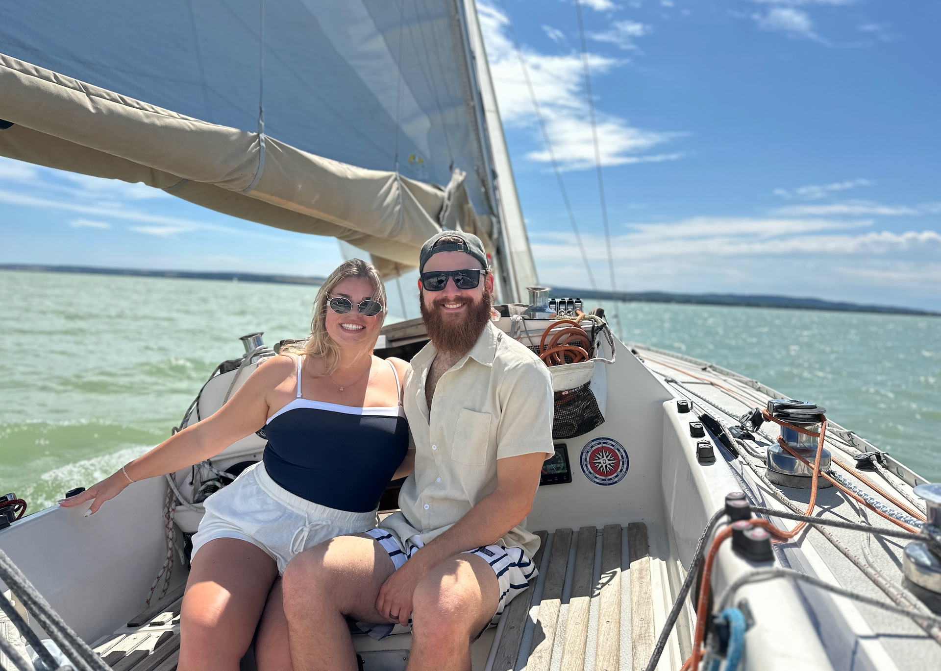 Couple on a sailboat enjoying a sunny day, blue water, and sky.