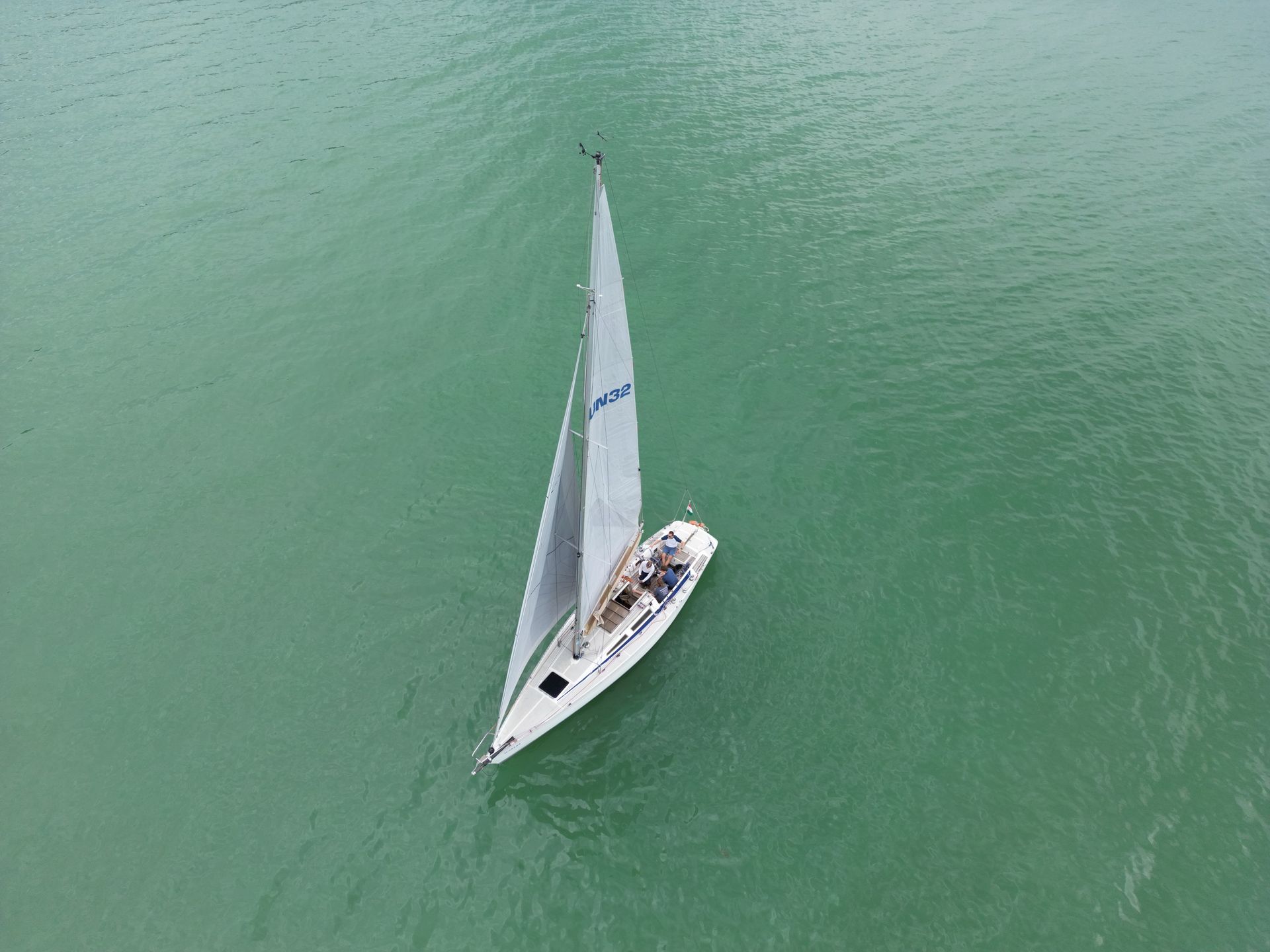 Sailboat on turquoise water with a raised sail; aerial view.