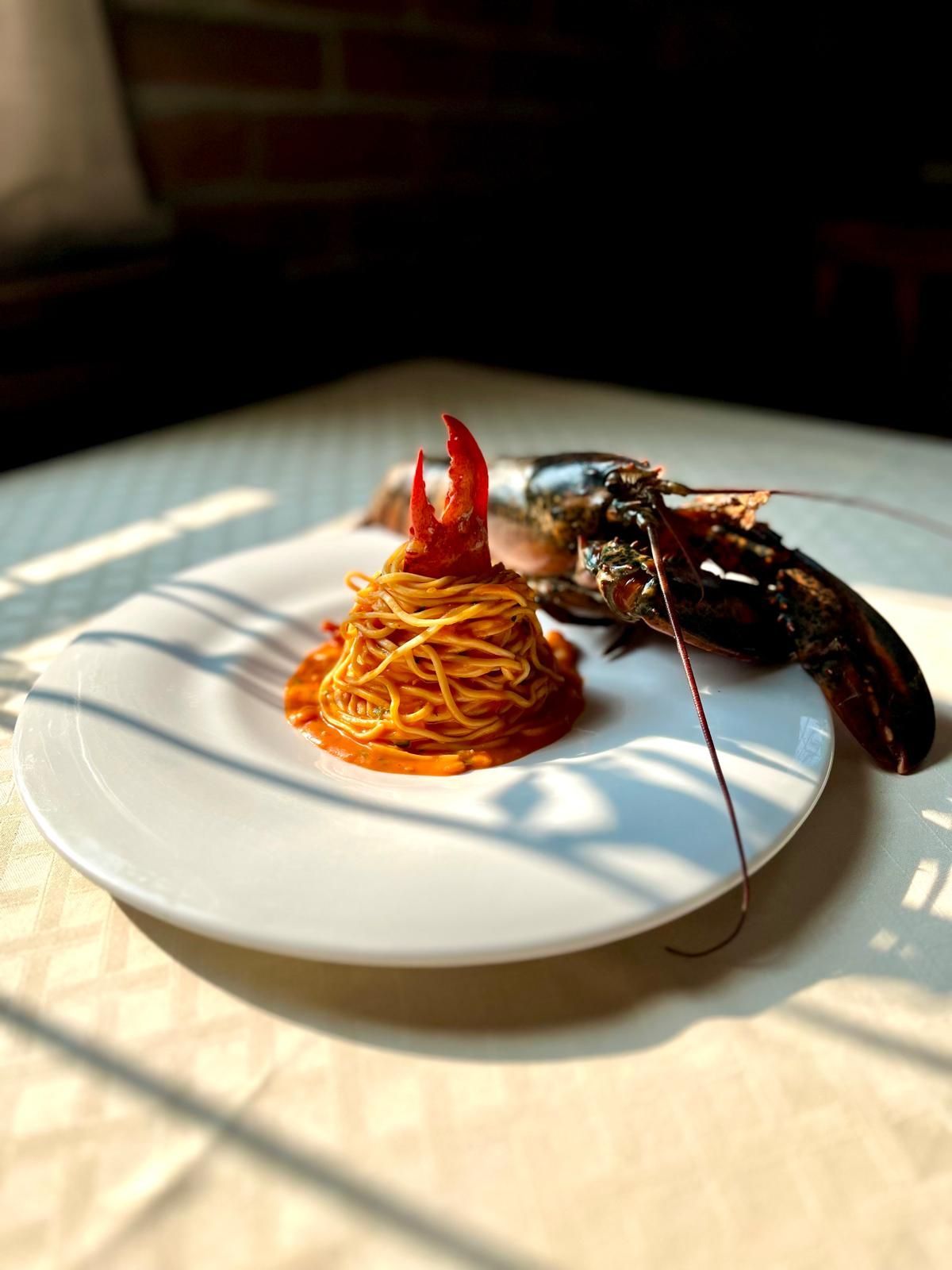 Spaghetti con chele d'aragosta su un piatto bianco, accanto all'aragosta intera. Ben illuminato in un ambiente da pranzo.