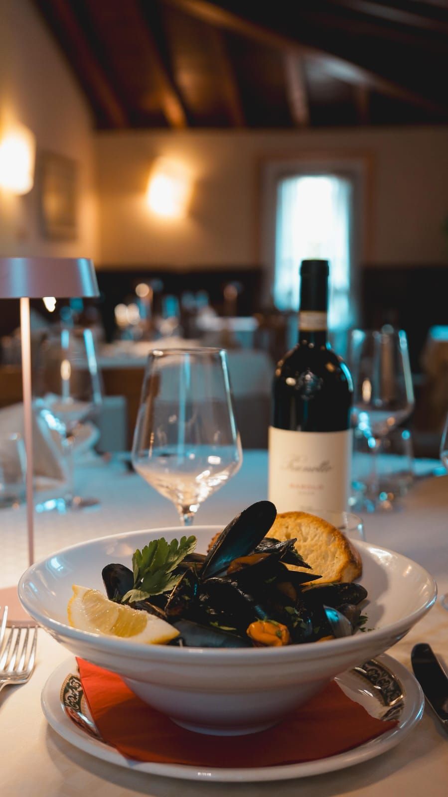 Cozze in una ciotola bianca con una bottiglia di vino e un bicchiere di vino su un tavolo in un ristorante.