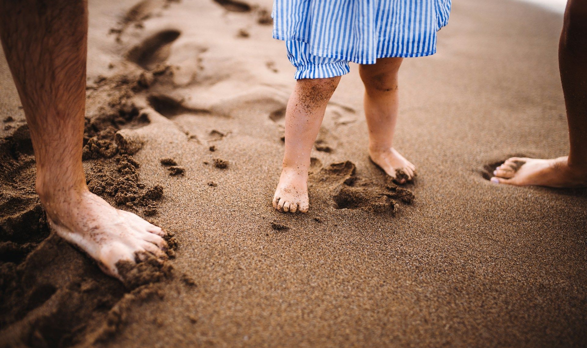 A man and a little girl are walking barefoot on the beach.
