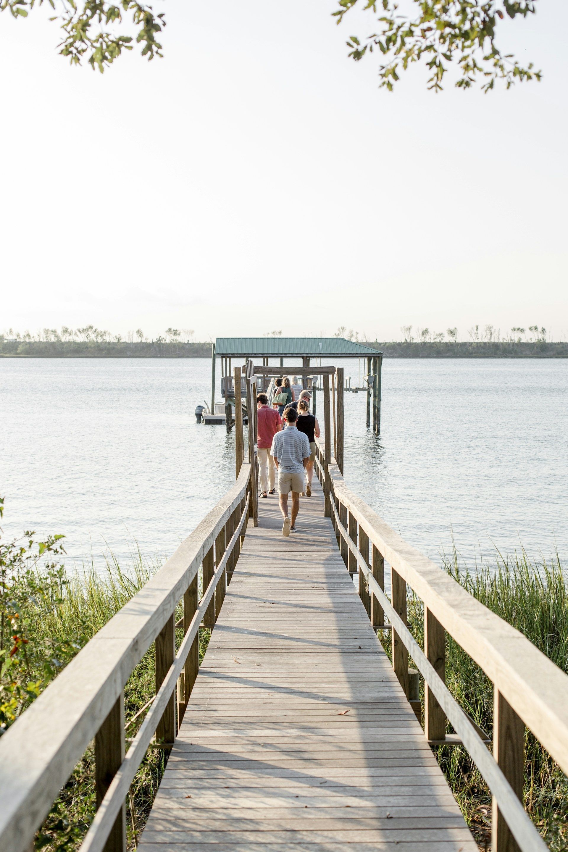 A group of people are walking down a wooden pier overlooking a body of water.