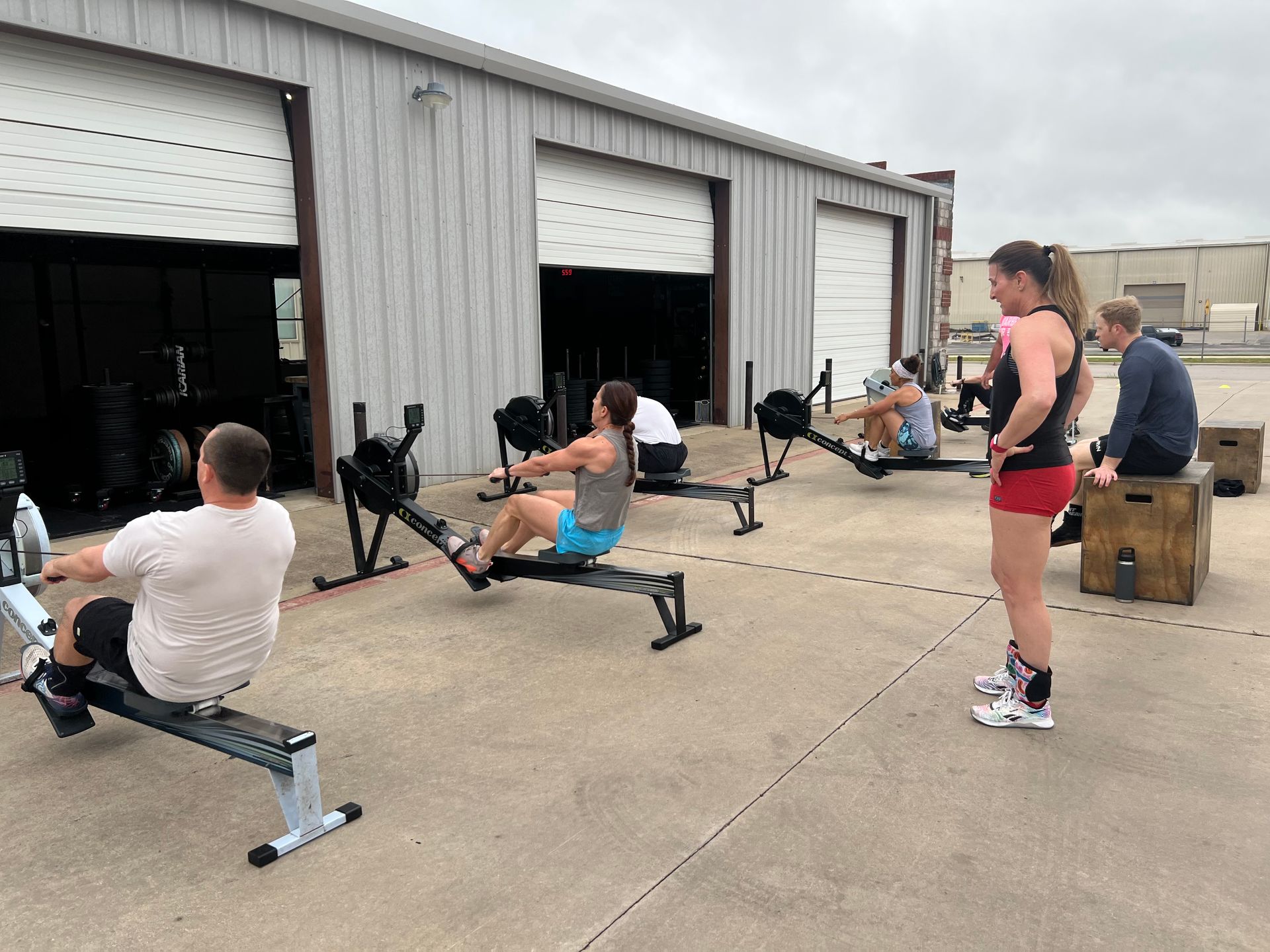 A group of people are doing exercises on rowing machines outside of a building.