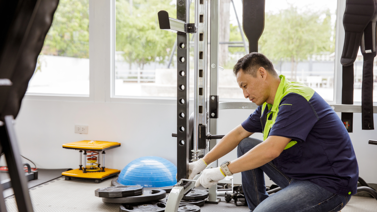 A man is kneeling down in a gym working on a machine.