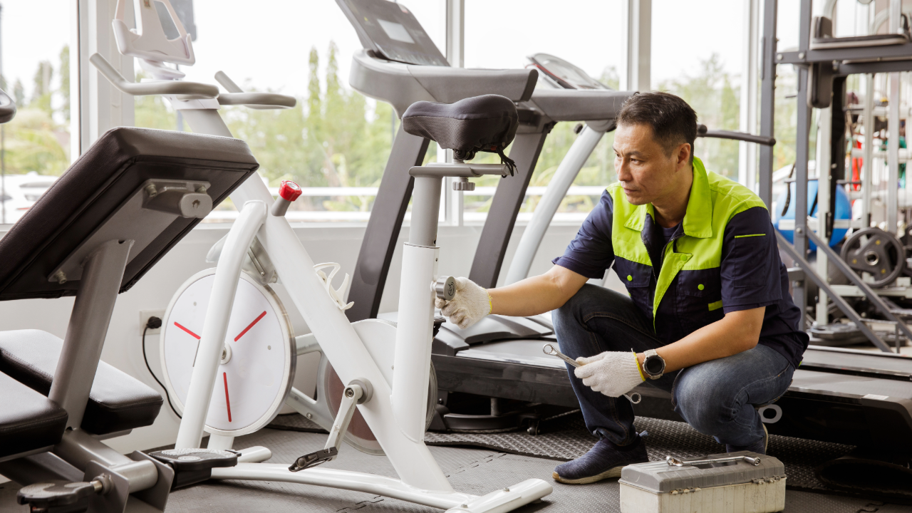 A man is repairing an exercise bike in a gym.