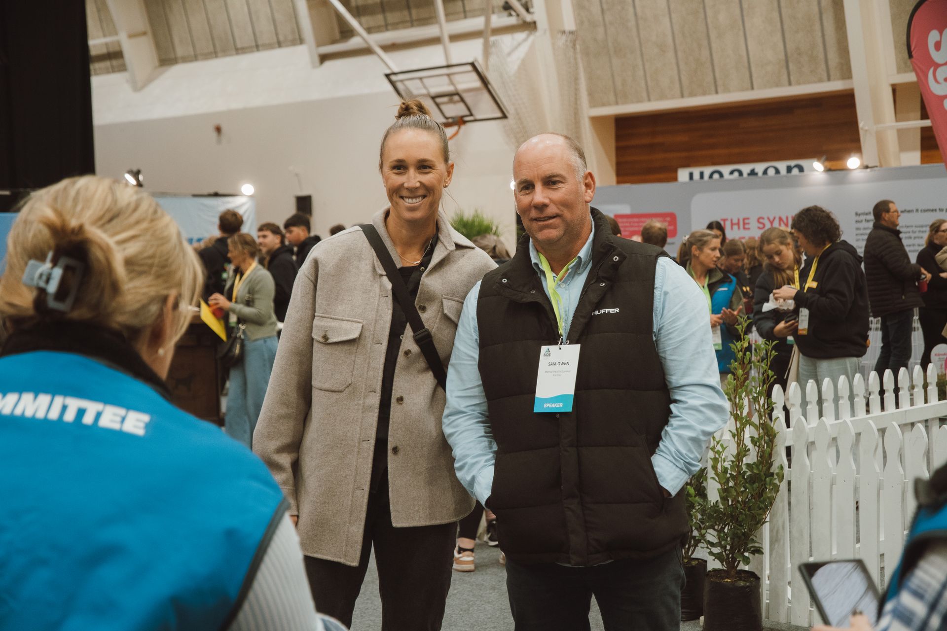 Two people pose for a photo with a volunteer. Indoors, convention or fair setting.