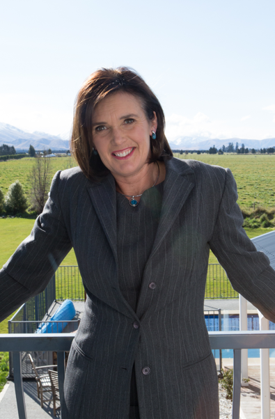 Man in a DairyNZ shirt smiles in a green field with black and white cows grazing in the background.