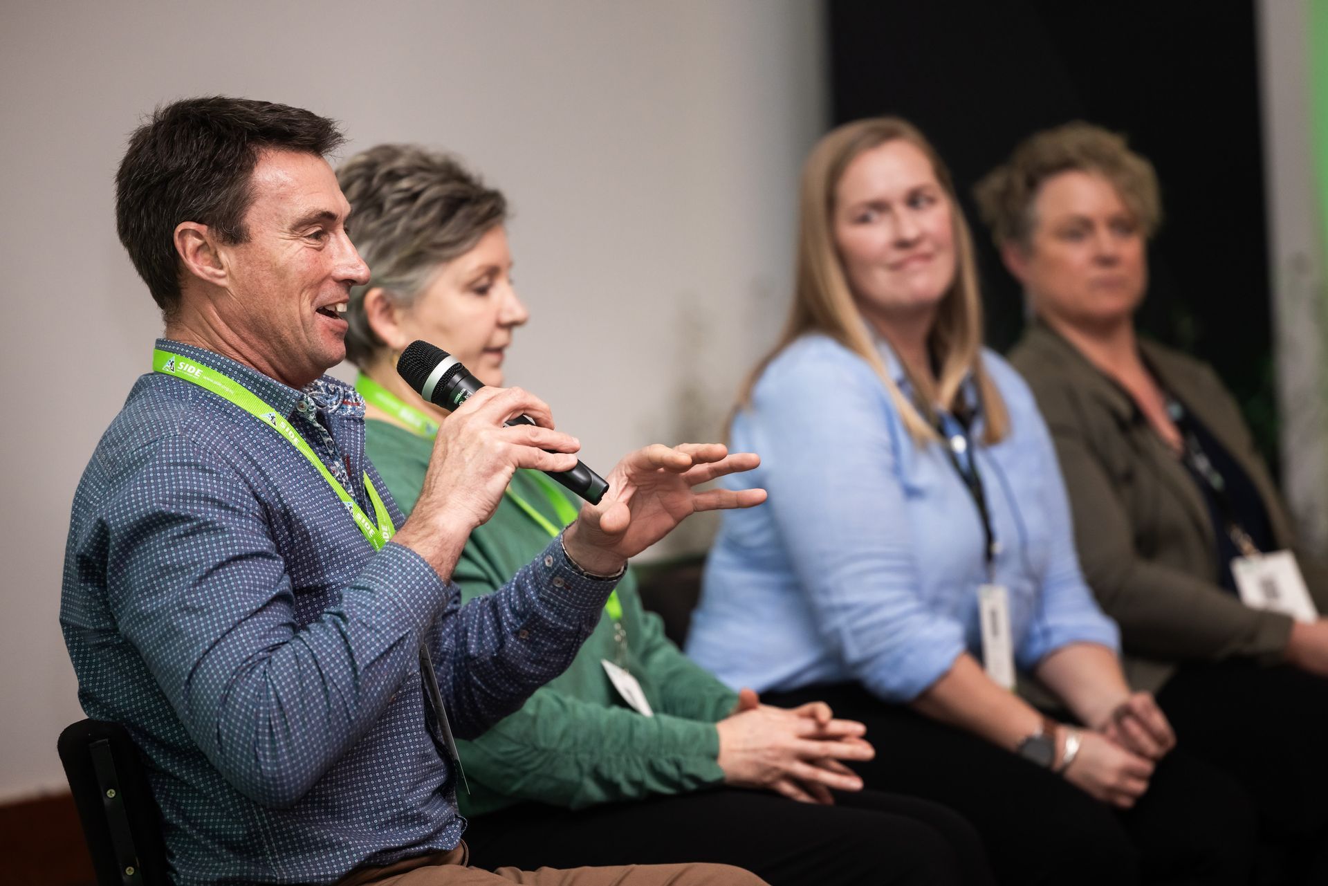Panel of four people seated, one man speaks into a microphone, gesturing with his hands. Others listen.