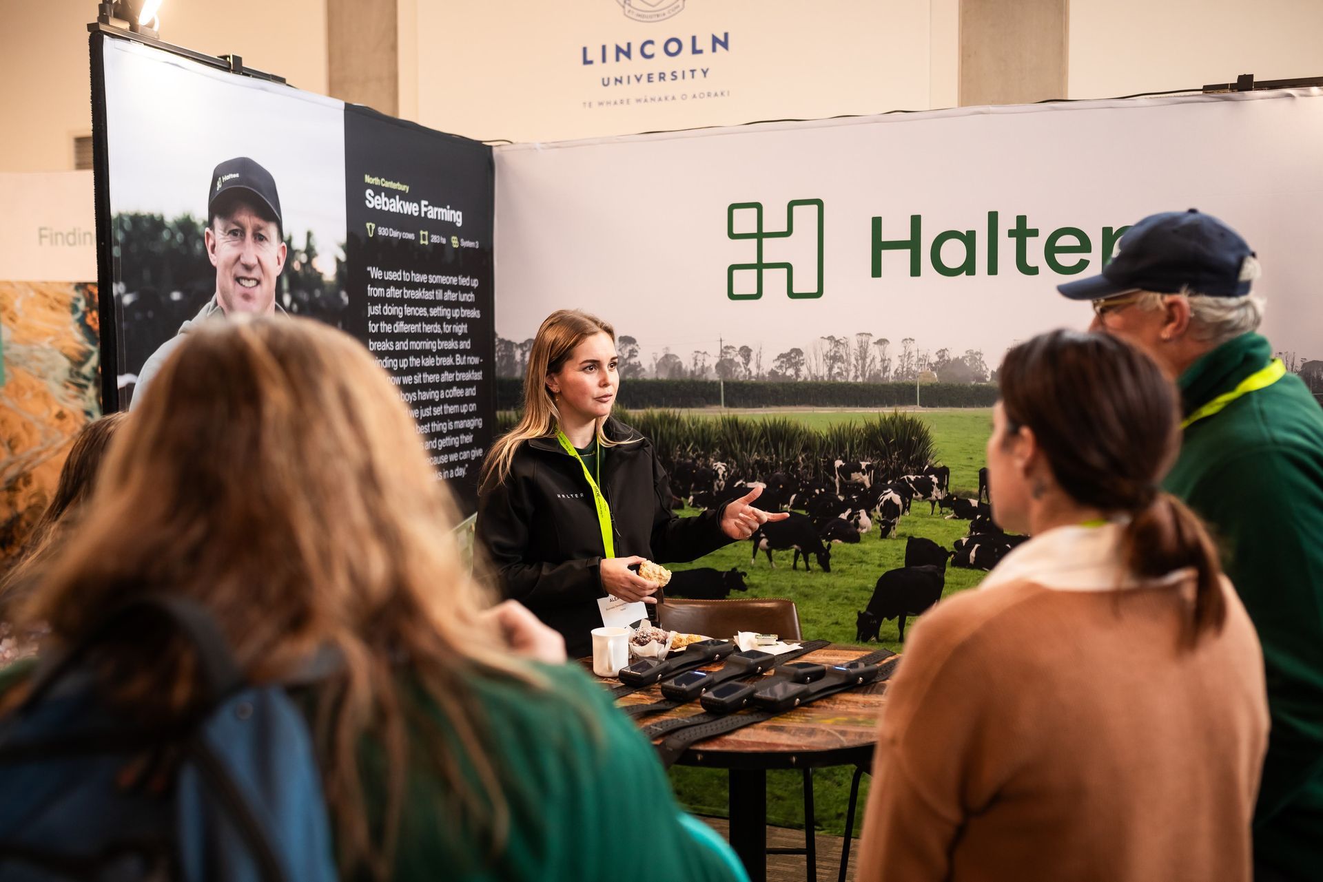 A woman speaks at a Halter booth at an event. People listen, and there's a backdrop with cows.