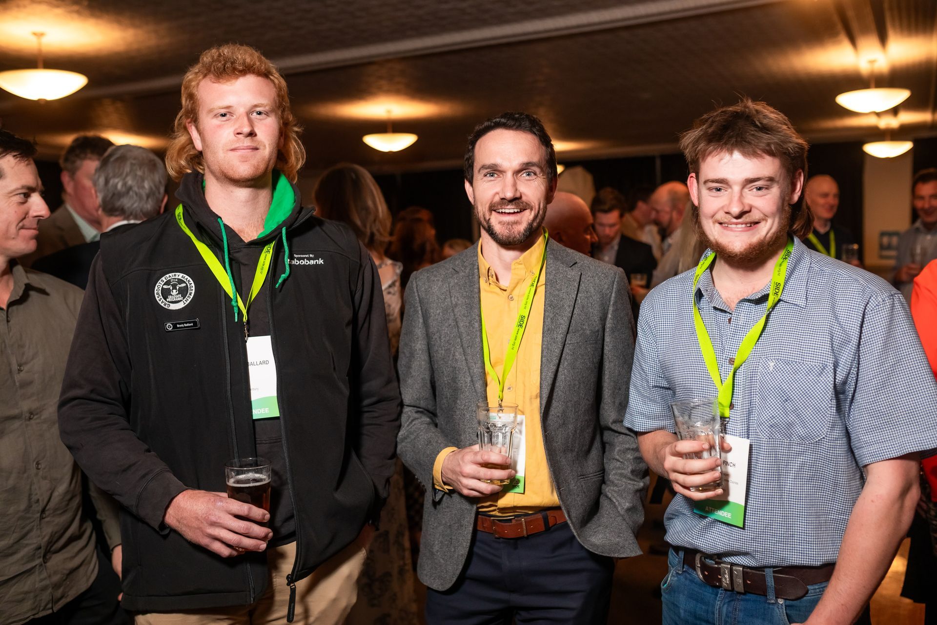 Three men at an event, holding drinks, smiling.
