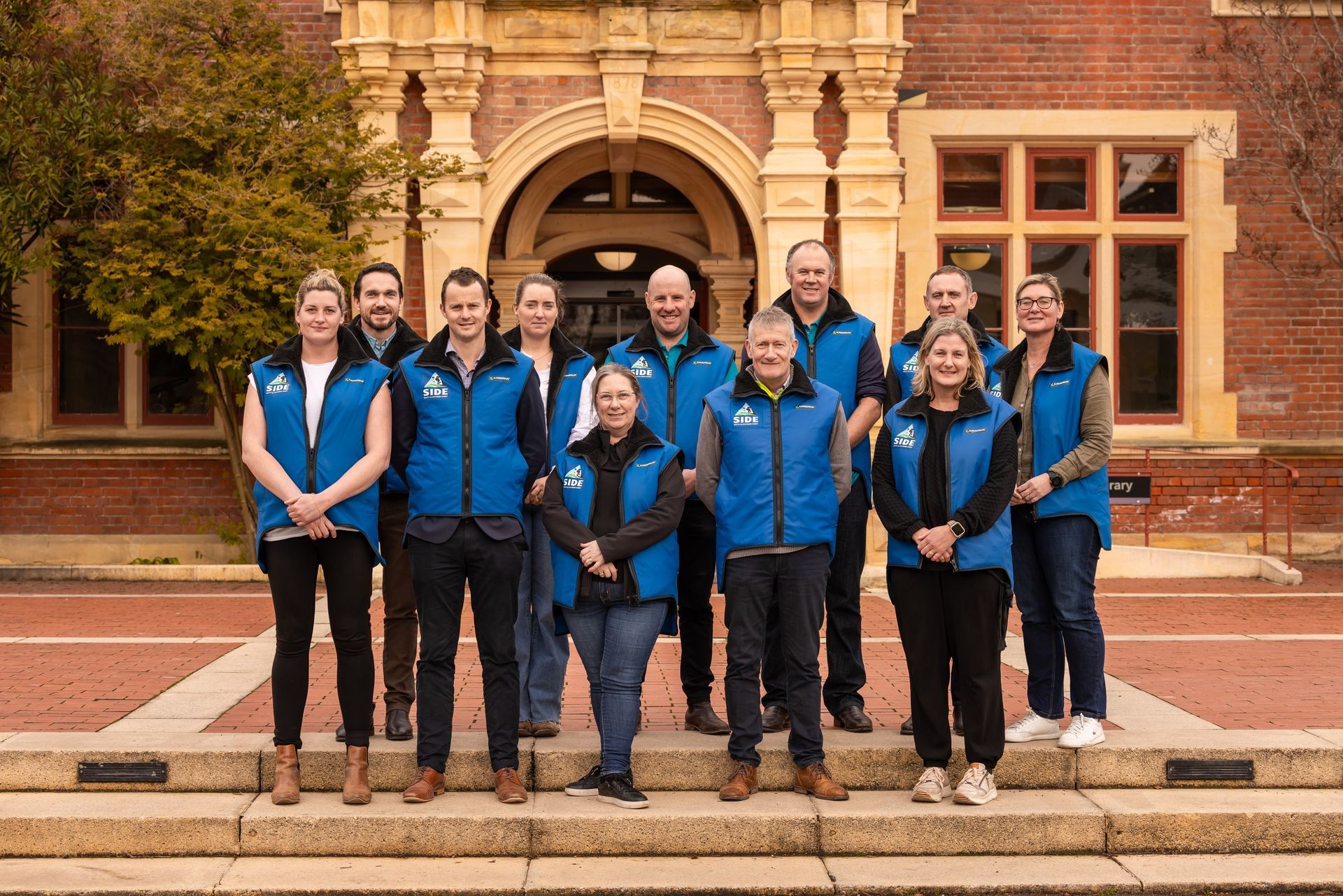 Group of people in blue vests standing on steps in front of a brick building.
