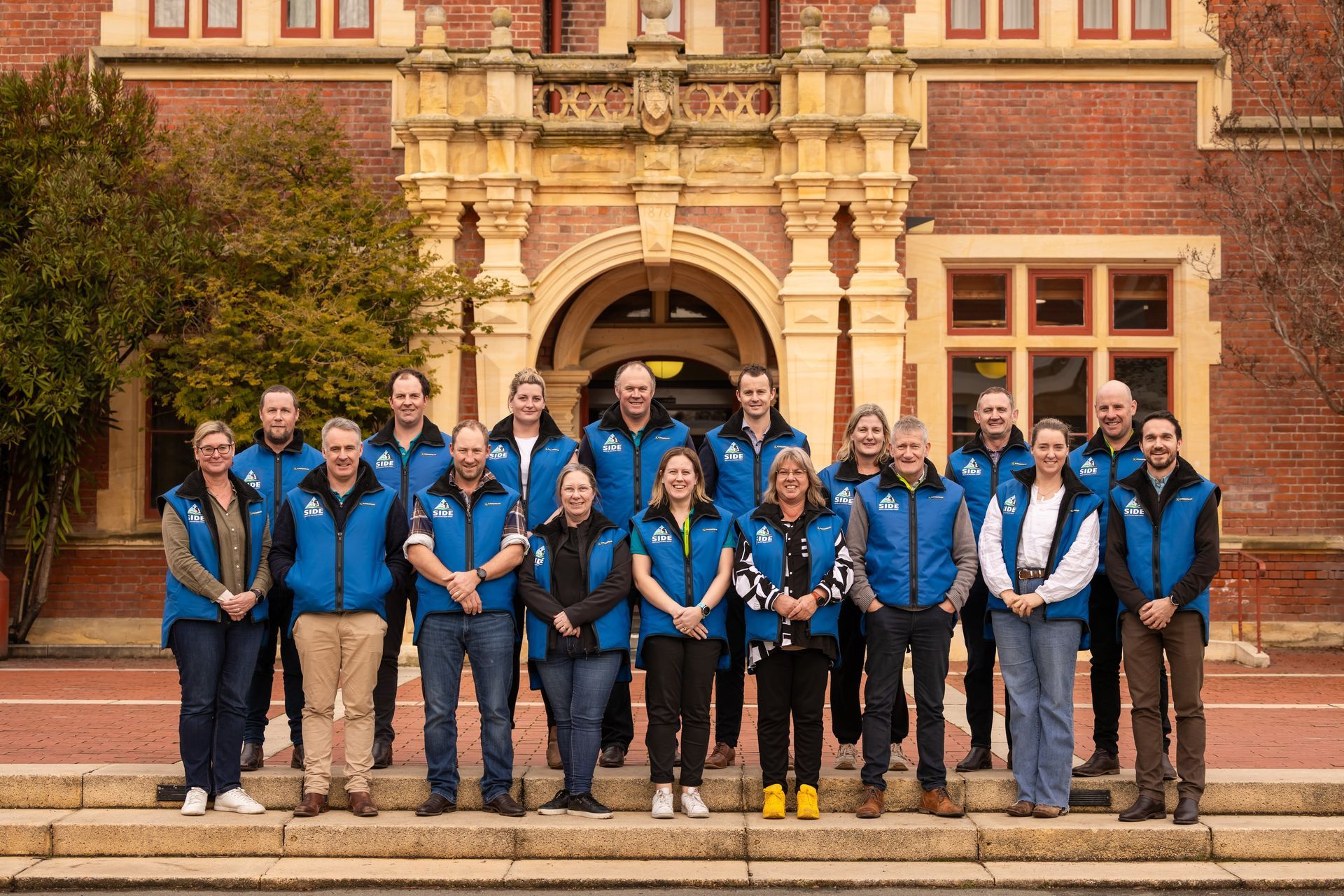 Group of people in blue vests standing on steps in front of a brick building.