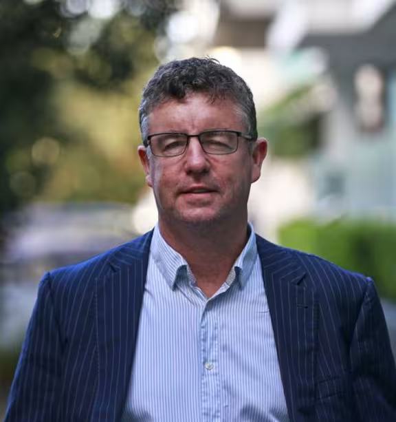 Man in glasses and blue blazer, standing outdoors.