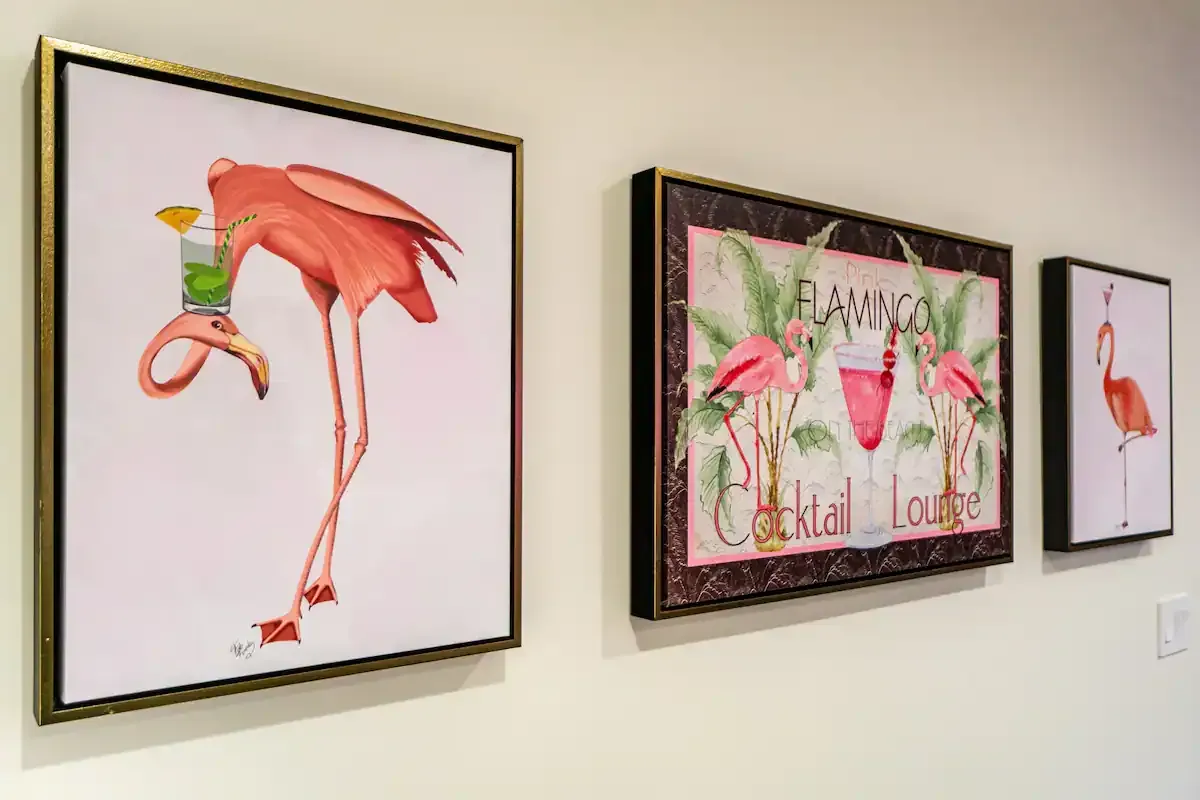Three framed paintings of flamingos are hanging on a wall.