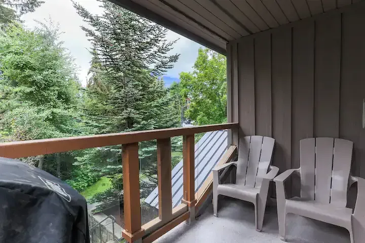 A balcony with two chairs and a grill with trees in the background