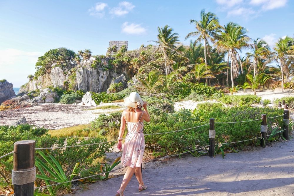 A woman in a dress and hat is walking down a path.
